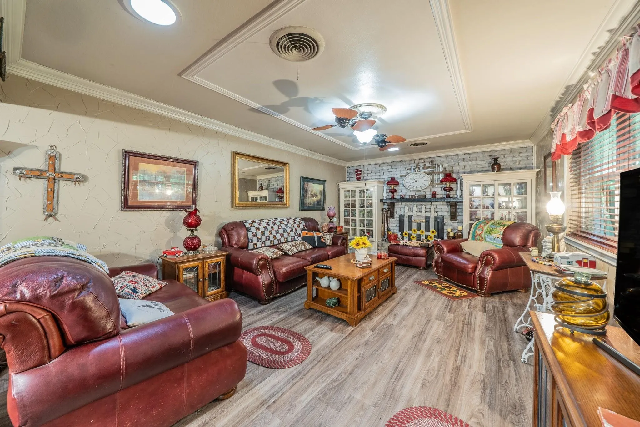 Living area featuring wood-finish flooring, a painted brick fireplace, built-in glass-front cabinetry, recessed ceiling lighting, and crown molding