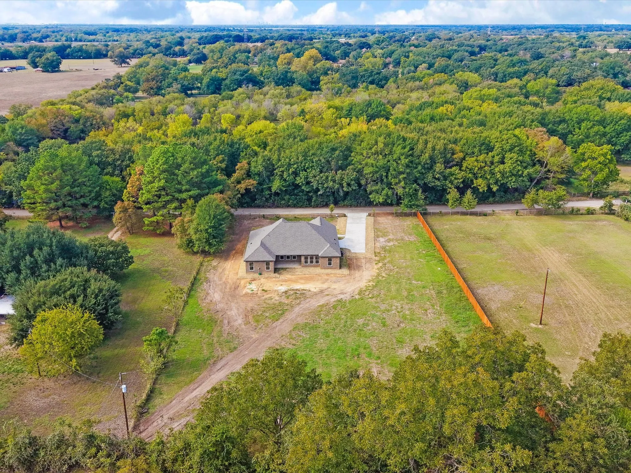 Single-story residence featuring a multi-gable roofline, exterior brick masonry, concrete driveway, and expansive acreage bordered by mature trees and wood fencing