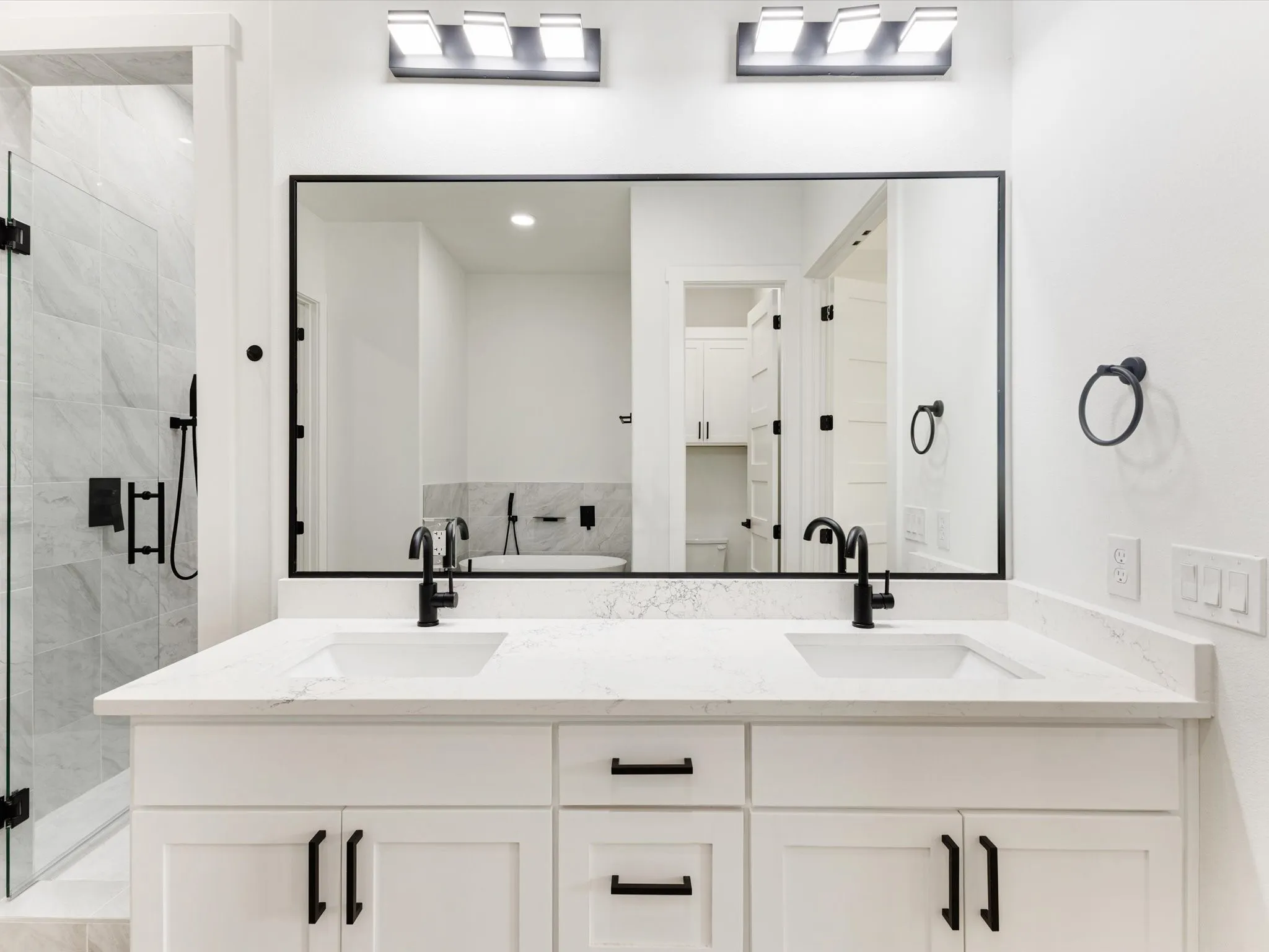 Dual-sink vanity with white cabinetry, stone-finish countertop, matte black hardware, integrated rectangular basins, and a large rectangular mirror framed in black
