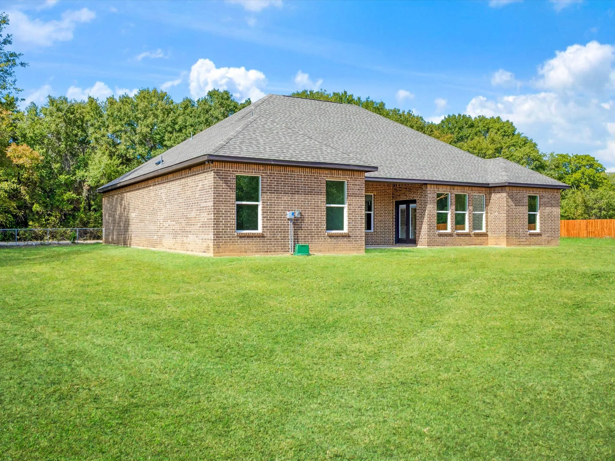 Single-story brick exterior featuring a hipped roof, multi-pane windows, and a sprawling grass yard with perimeter tree growth