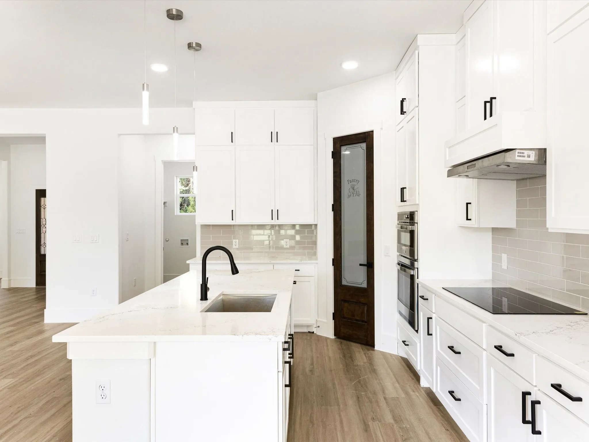 Kitchen featuring white cabinetry, quartz countertops, a central island with a matte black faucet, integrated stainless steel double wall ovens, and wood-finish flooring
