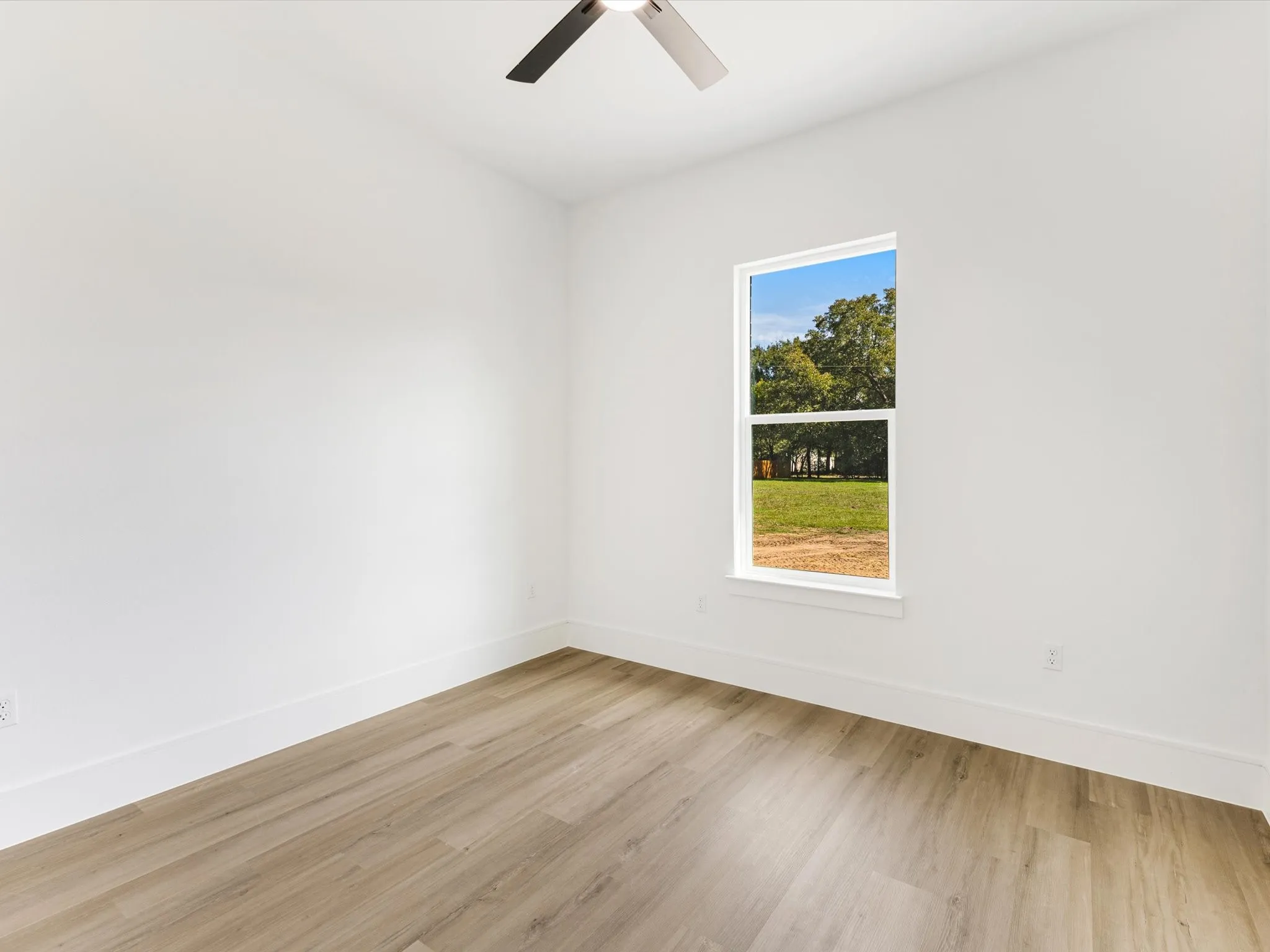 Neutral interior space featuring wood-finish flooring, a ceiling fan, and a single-hung window
