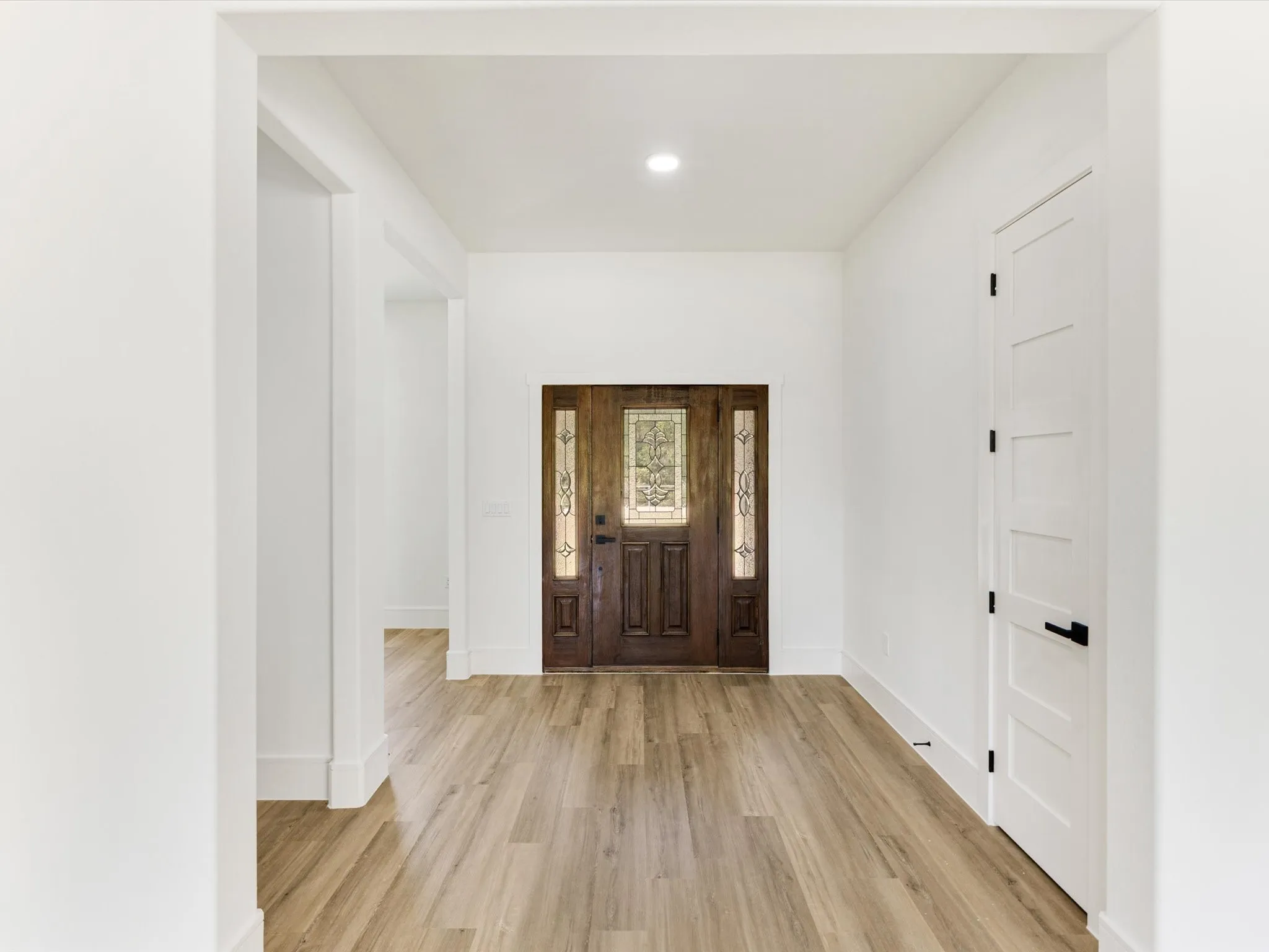 Entryway featuring wood-finish flooring, a solid wood-stain entry door with decorative glass inserts, and a white five-panel interior door with matte black hardware