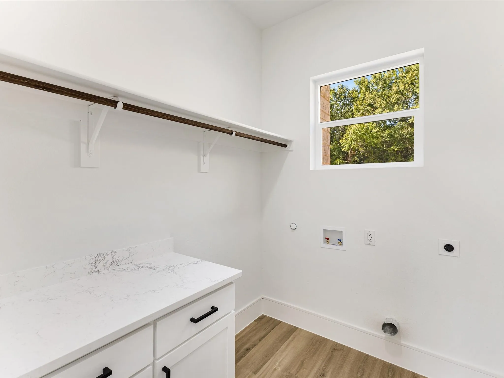 Utility room featuring white shaker-style cabinetry, a stone-patterned countertop, wood-finish flooring, a wall-mounted hanging rod, and a window