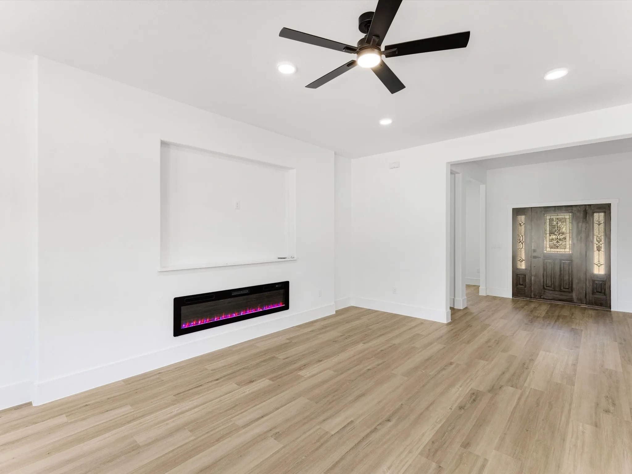 Interior space featuring wood-finish flooring, a wall-mounted electric fireplace, recessed lighting, a ceiling fan with integrated lighting, and a front entry door with glass panel detailing