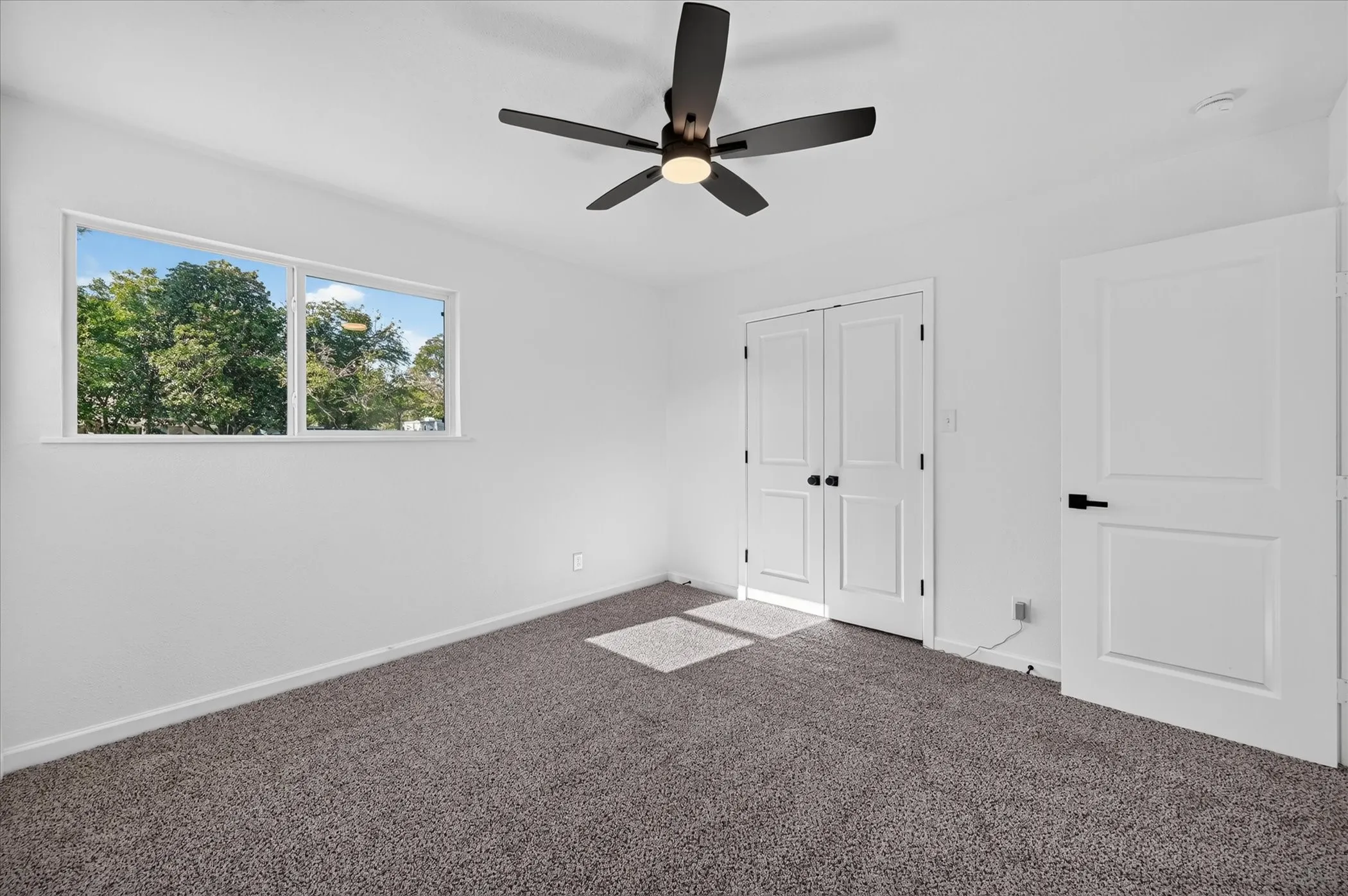 Interior space featuring neutral-toned carpeting, a horizontal sliding window, a matte black ceiling fan, and paneled doors with matching matte black hardware