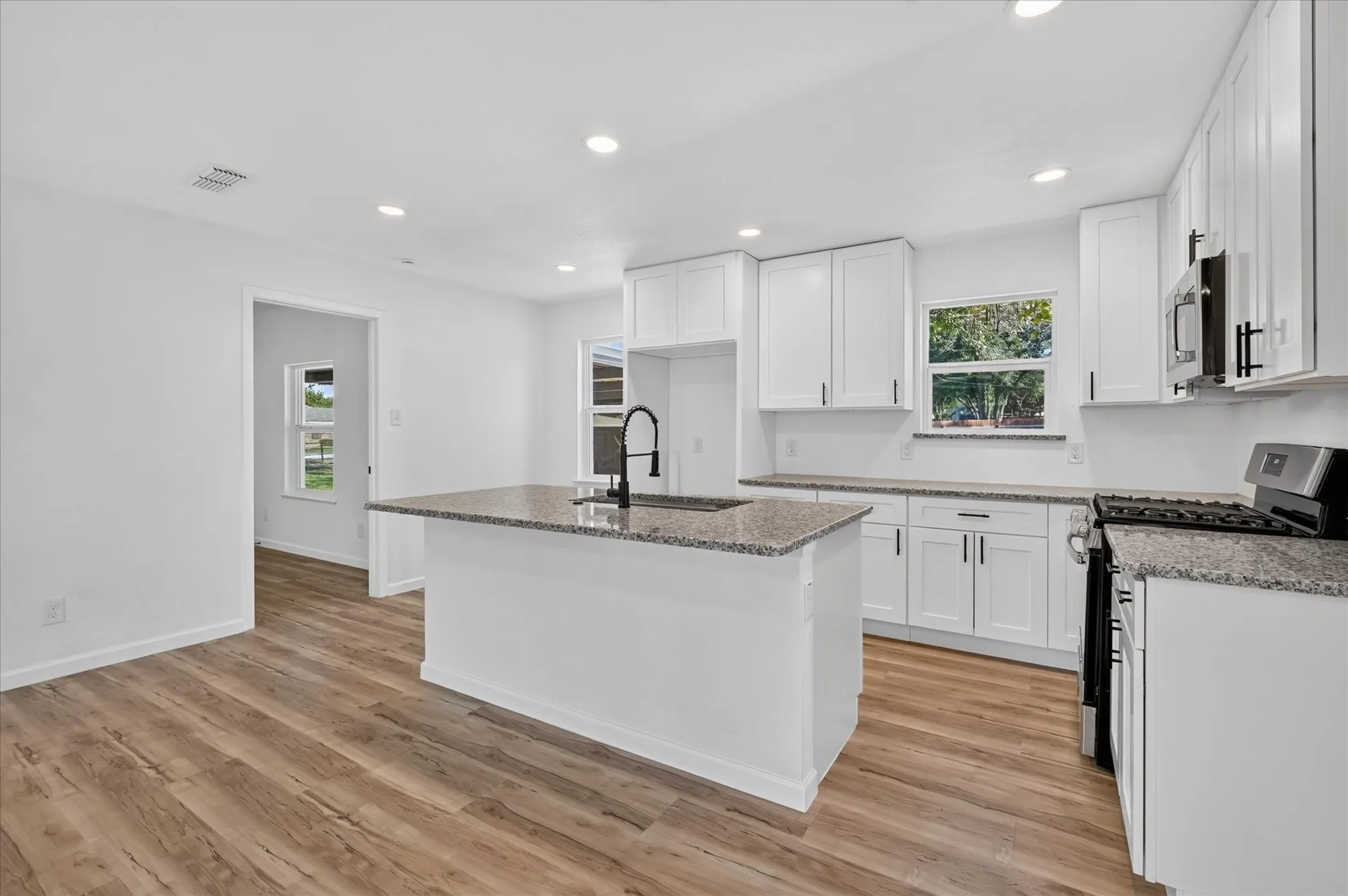 Kitchen featuring white cabinetry, stone-finish countertops, a central island with a gooseneck faucet, stainless steel appliances, and wood-finish flooring