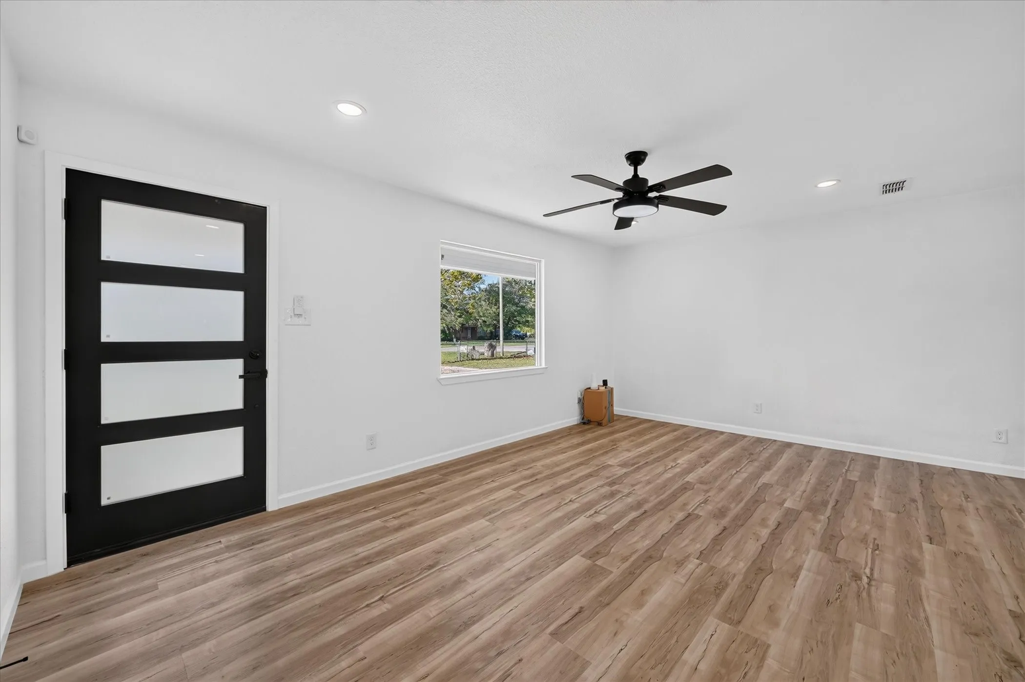 Room featuring wood-finish flooring, recessed lighting, matte black ceiling fan, and a contemporary entry door with frosted glass panels