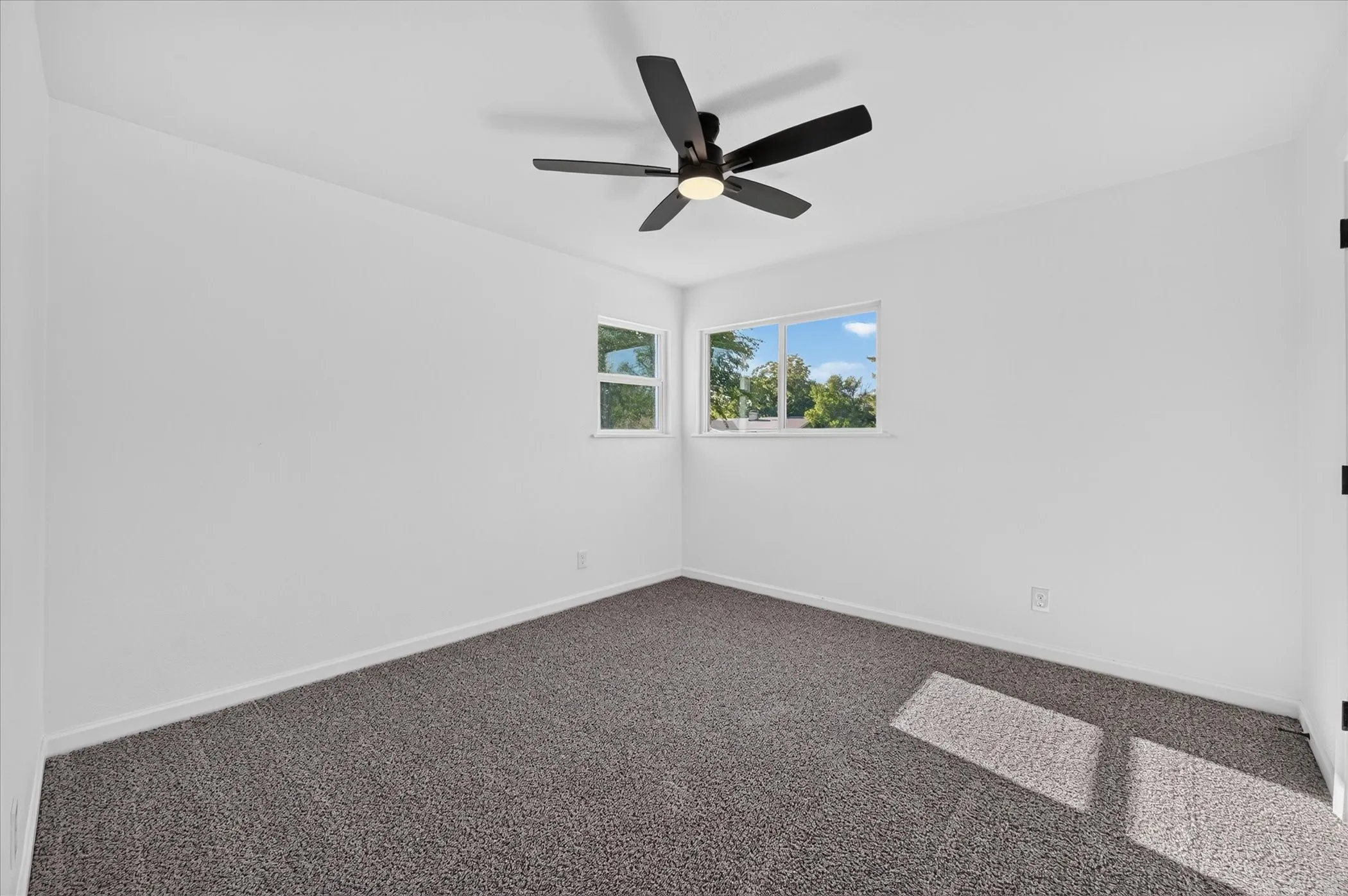 Neutral interior featuring wall-to-wall carpeting, dual-pane windows, and a multi-blade ceiling fan with integrated lighting