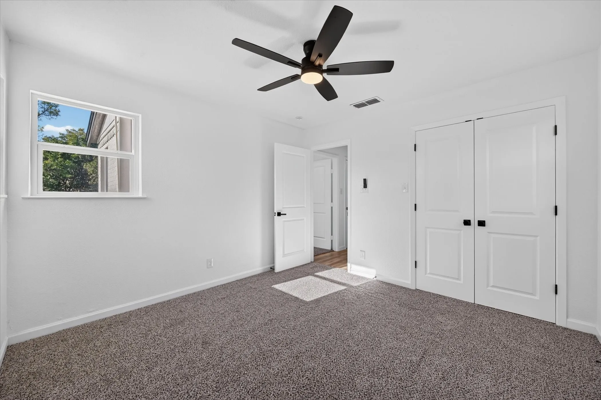 Room featuring neutral-toned carpeting, a five-blade ceiling fan with integrated lighting, dual-panel closet doors, and single-pane window