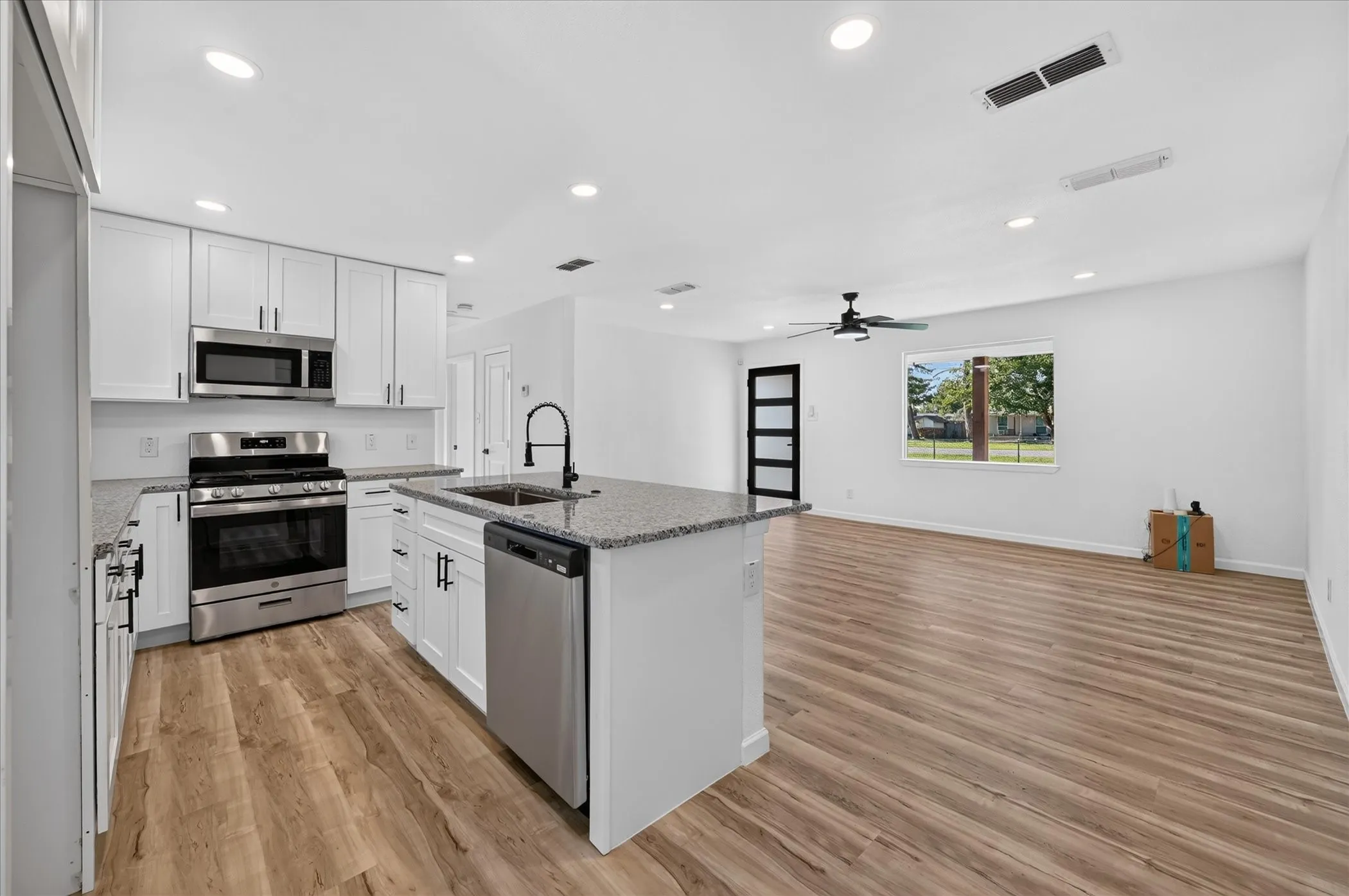 Kitchen featuring white shaker-style cabinetry, stone-finish countertops, stainless steel appliances, a center island with a high-arch faucet, and wood-finish flooring