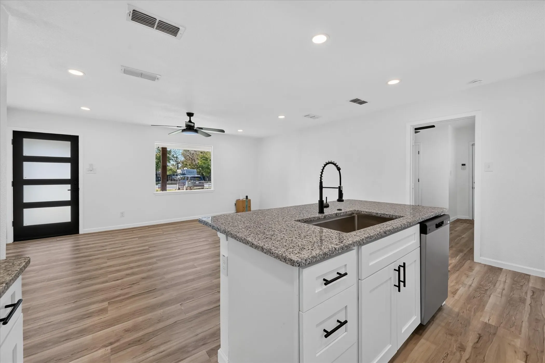 Kitchen island featuring stone countertops, a stainless steel undermount sink with a matte black pulldown faucet, and white cabinetry with matte black hardware, complemented by wood-finish flooring throughout