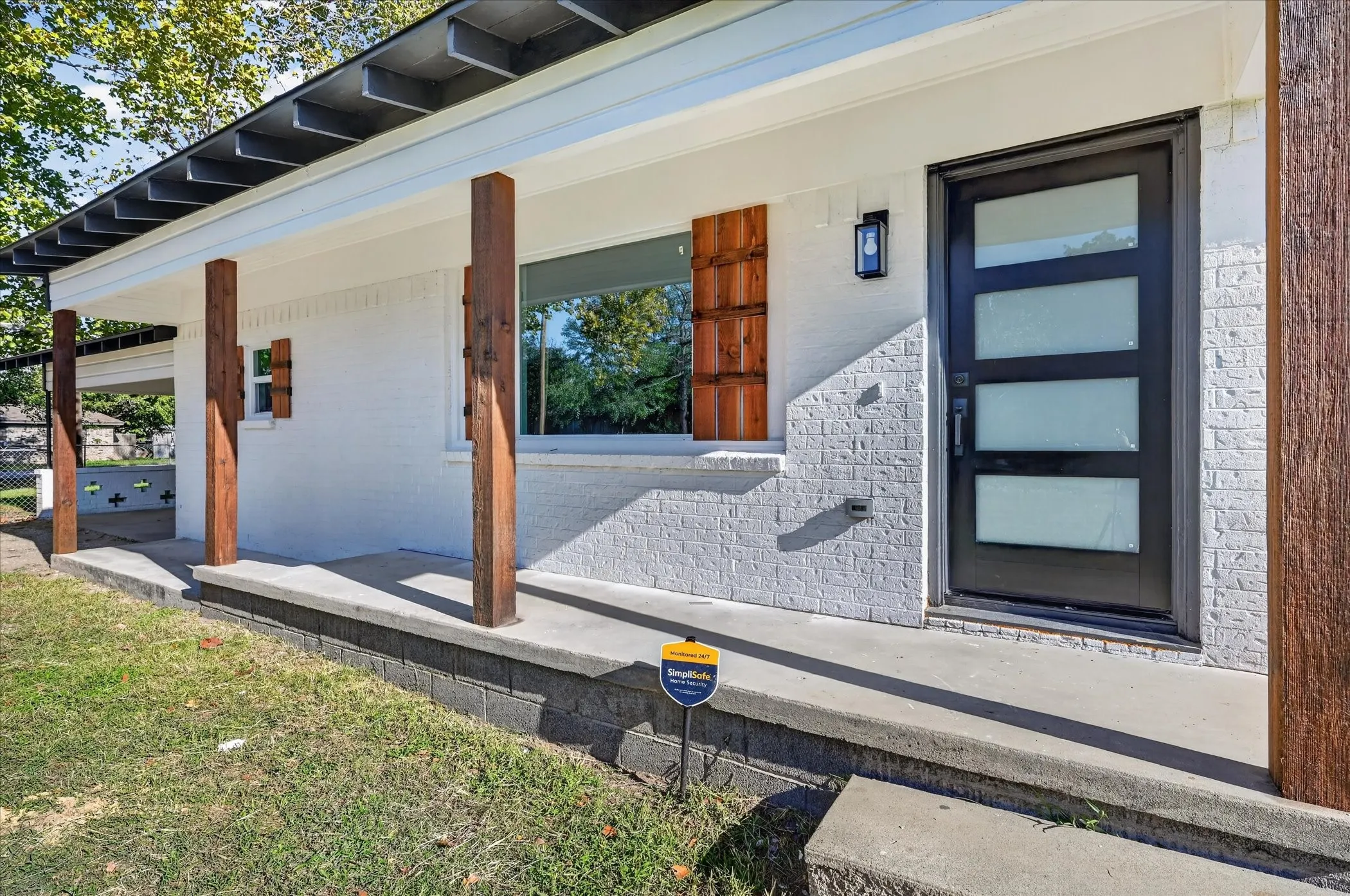 Exterior facade featuring white painted brick, a concrete covered porch with square timber support posts, horizontal wood-slat shutters, and a modern glass-panel front door