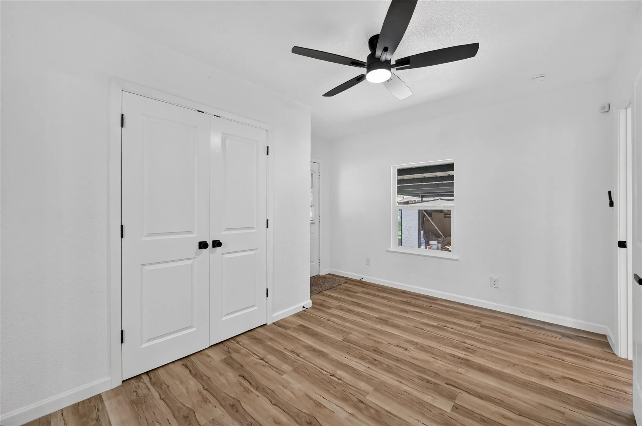 Wood-finish flooring, double-door closet with matte black hardware, and a contemporary ceiling fan with integrated lighting