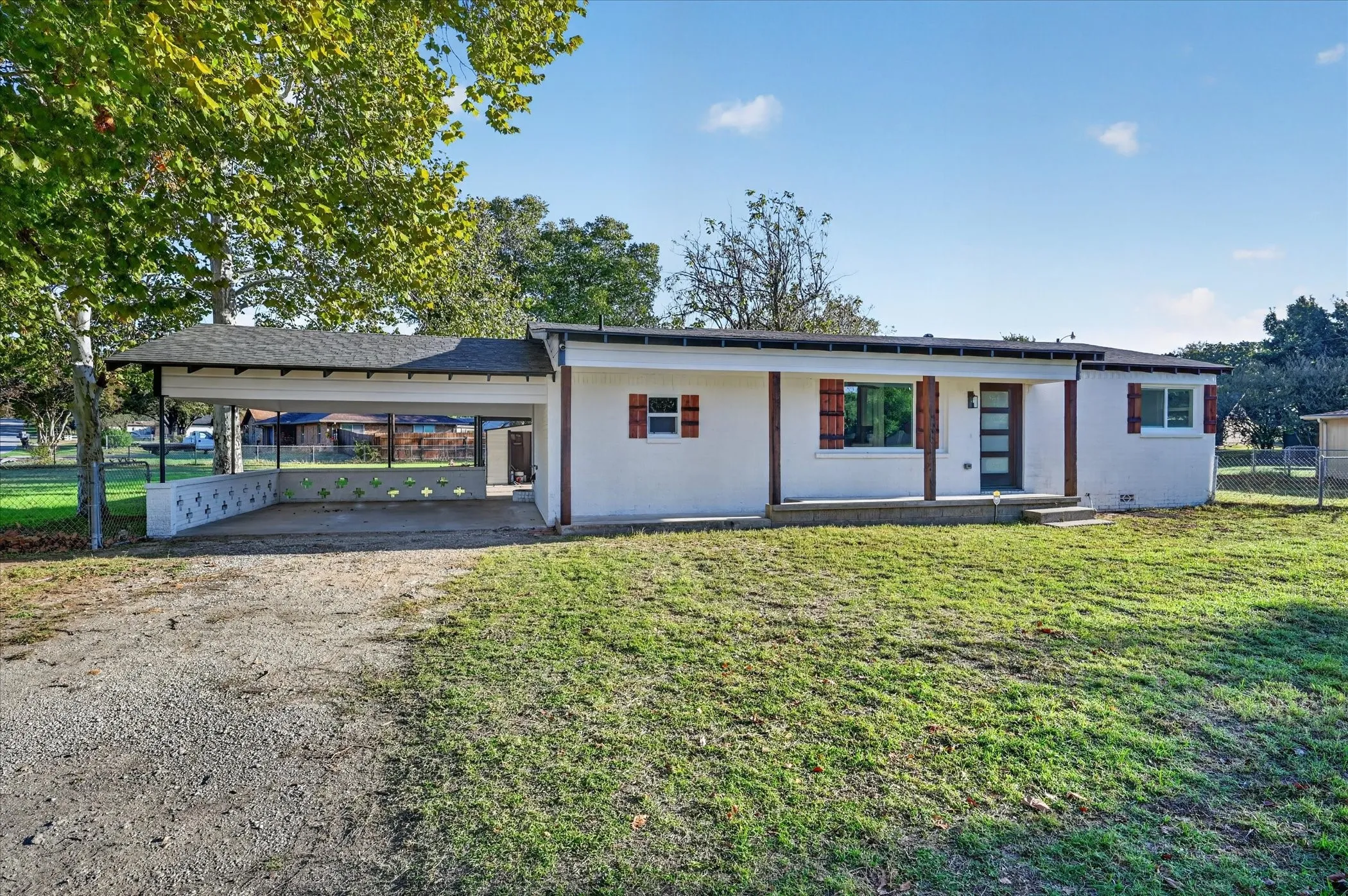 Single-story exterior featuring a light-colored brick, covered carport with decorative masonry screening, and wood-finish window shutters