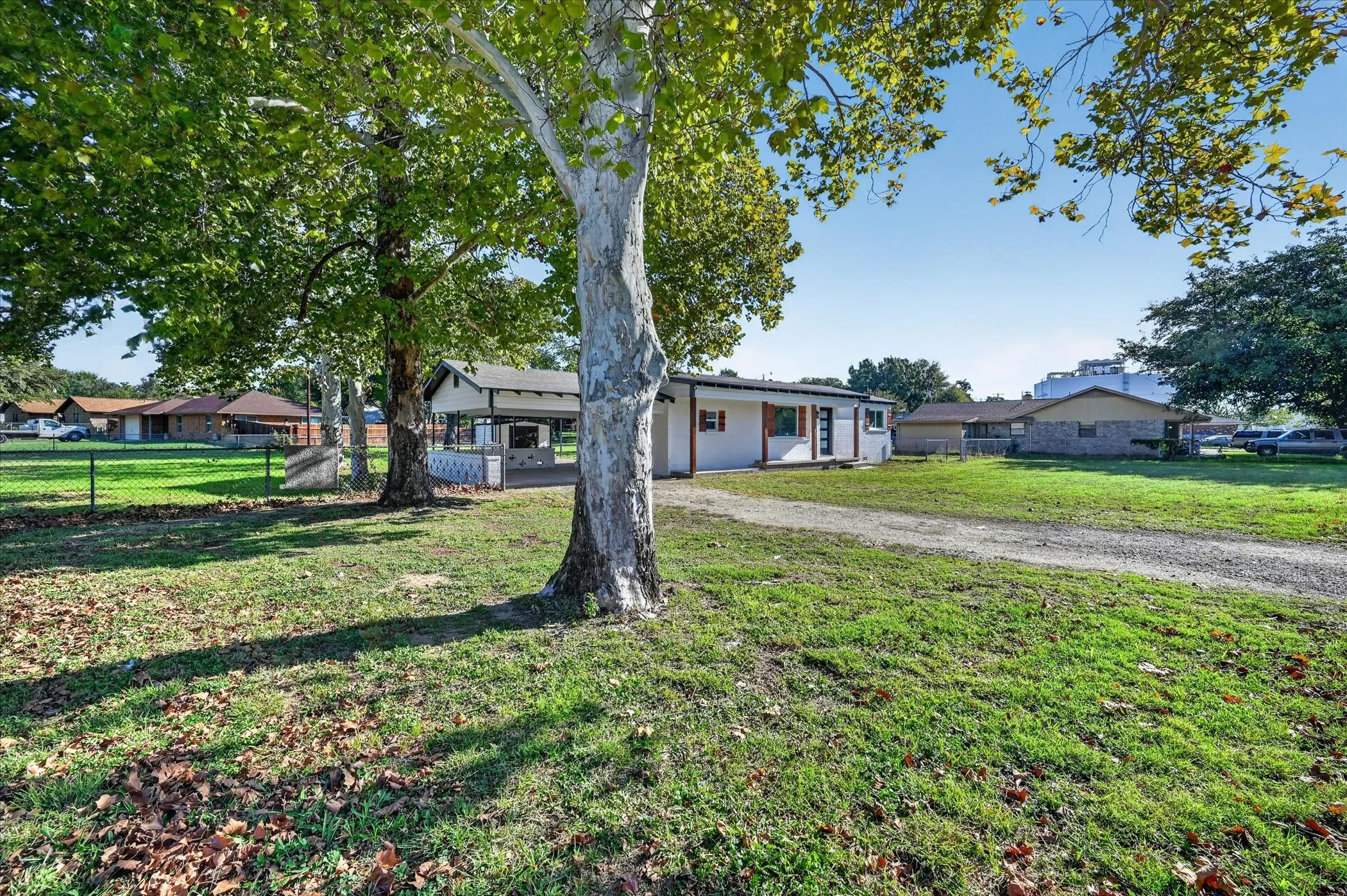 Expansive lot featuring mature trees, a graveled driveway, and a covered patio area