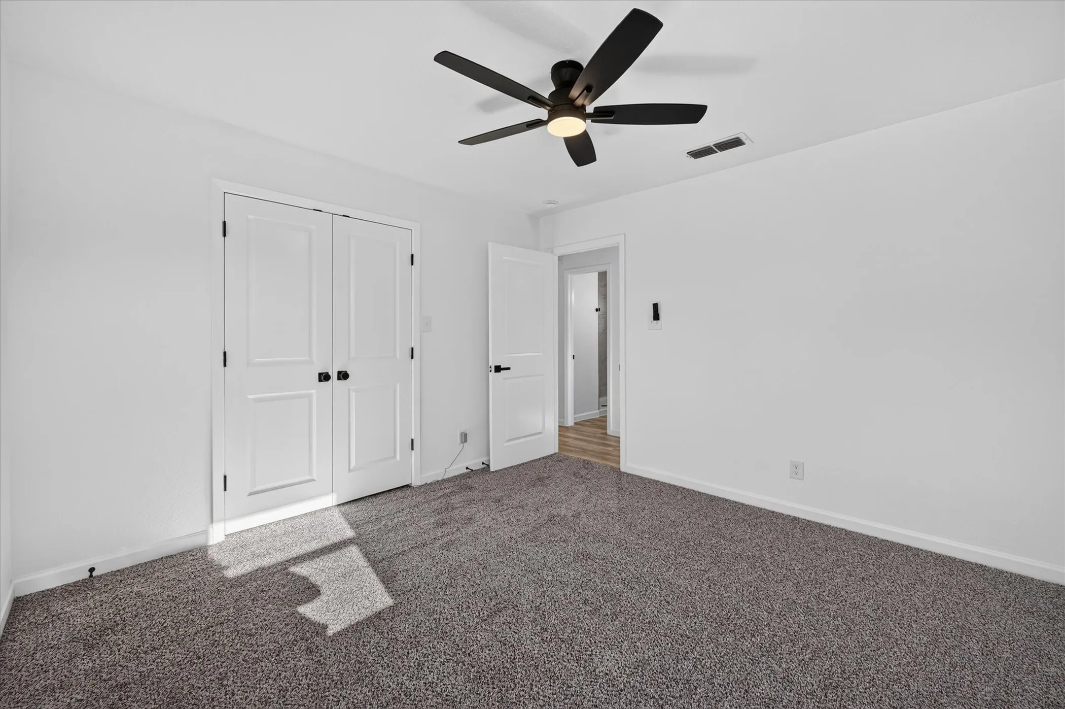 Room featuring neutral-toned carpeting, matte black hardware on doors, a black ceiling fan with integrated lighting, and white interior doors