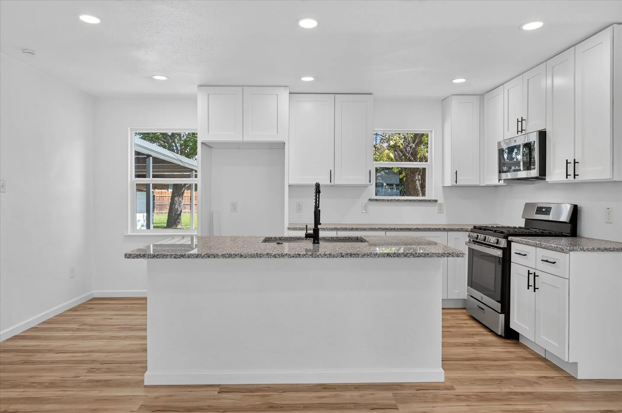 Kitchen featuring white shaker cabinetry, stone-patterned countertops, a center island with a matte black faucet, stainless steel appliances, and wood-finish flooring
