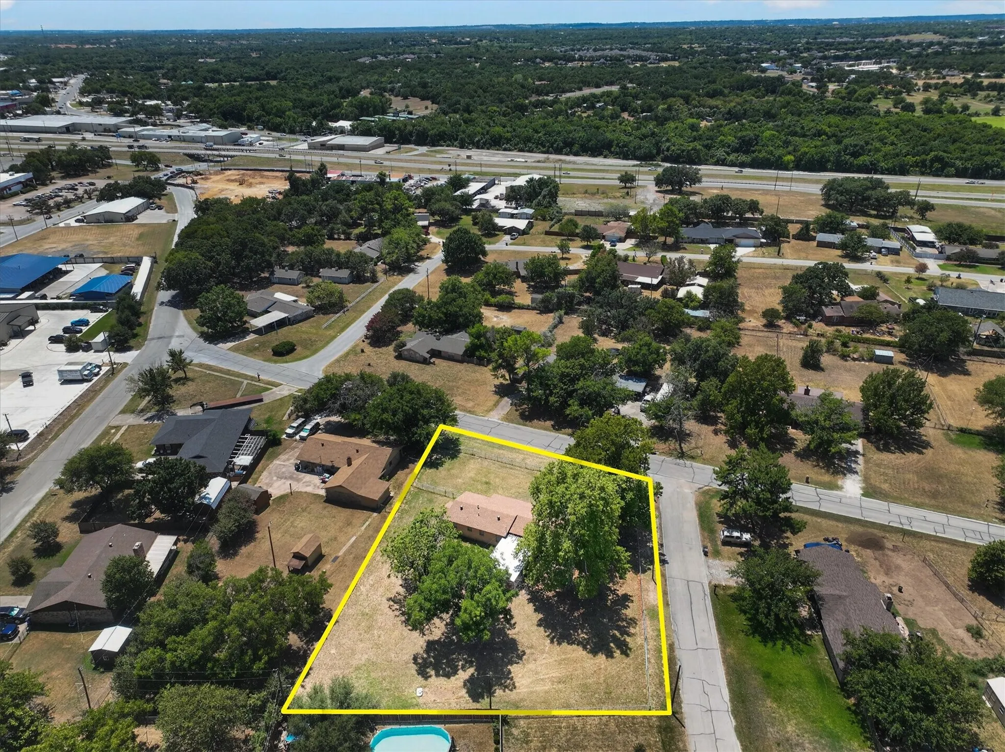Aerial view of a rectangular lot featuring a single-story residence, mature trees, and perimeter fencing