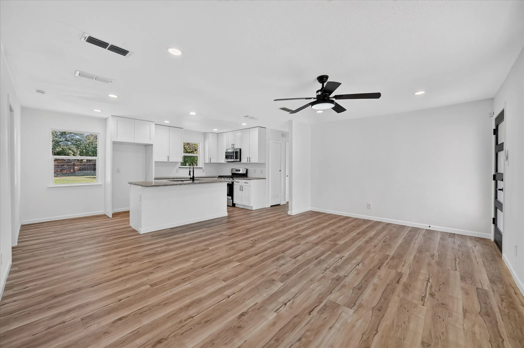 Open-concept interior featuring wood-finish flooring, recessed lighting, white cabinetry, stone-surface countertops, and a modern ceiling fan