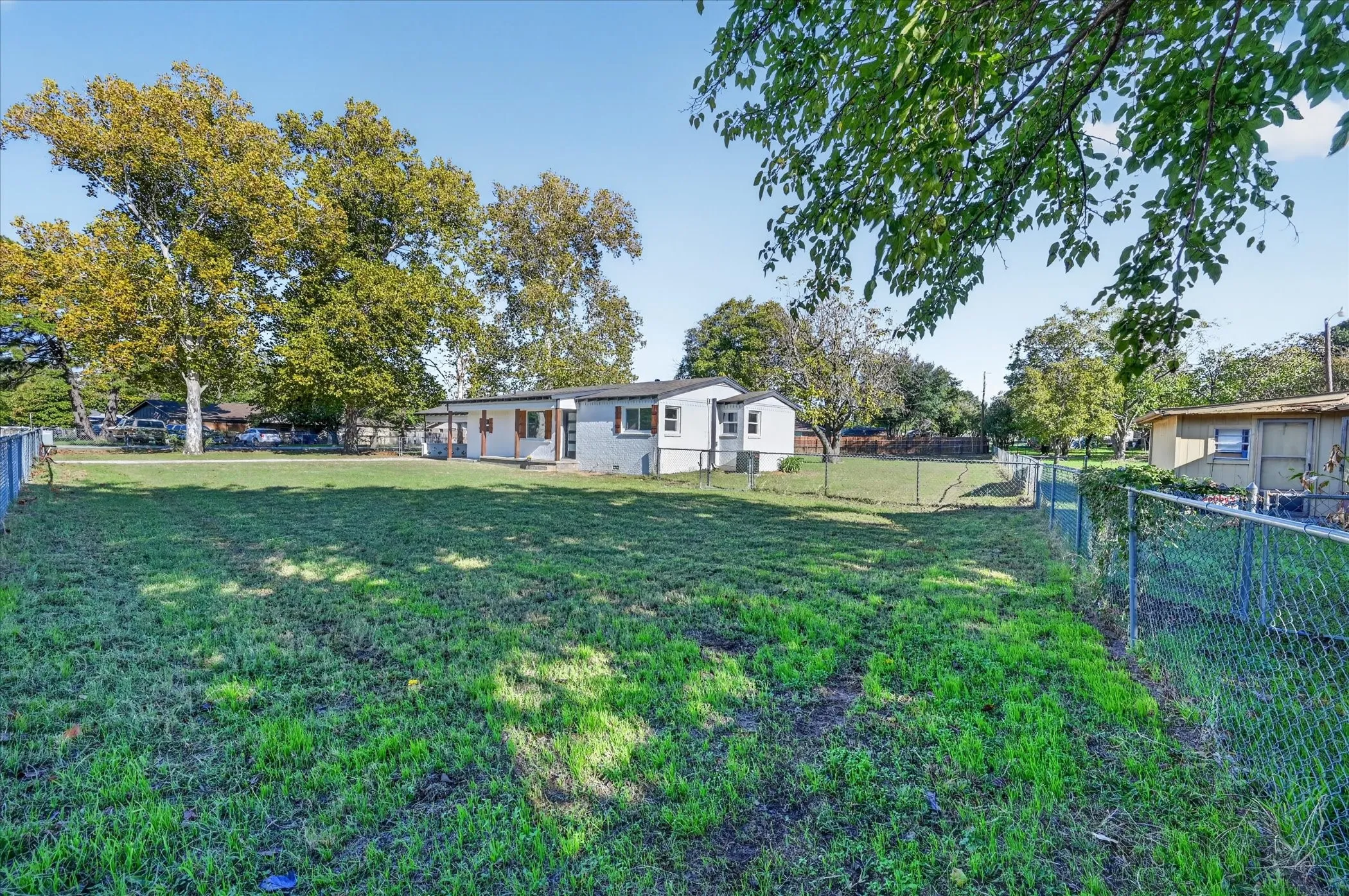 Expansive grounds featuring mature shade trees, chain-link perimeter fencing, and a detached storage structure