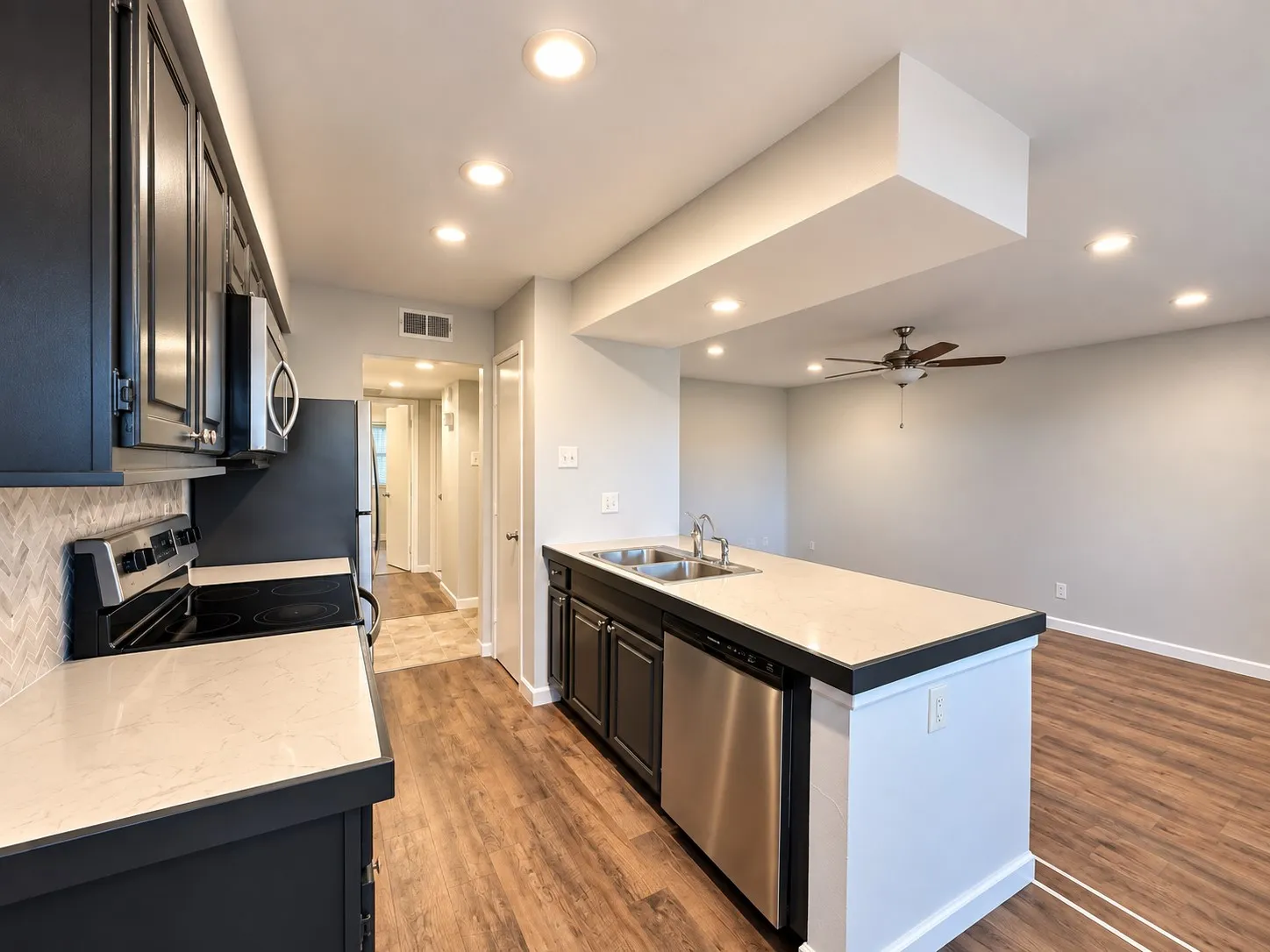 Kitchen featuring dark cabinetry, stone-finish countertops, herringbone-pattern tile backsplash, stainless steel appliances, and wood-finish flooring