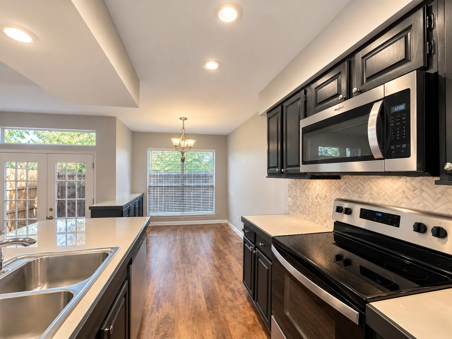 Kitchen featuring dark cabinetry, stainless steel appliances, herringbone-patterned tile backsplash, quartz countertops, and wood-finish flooring