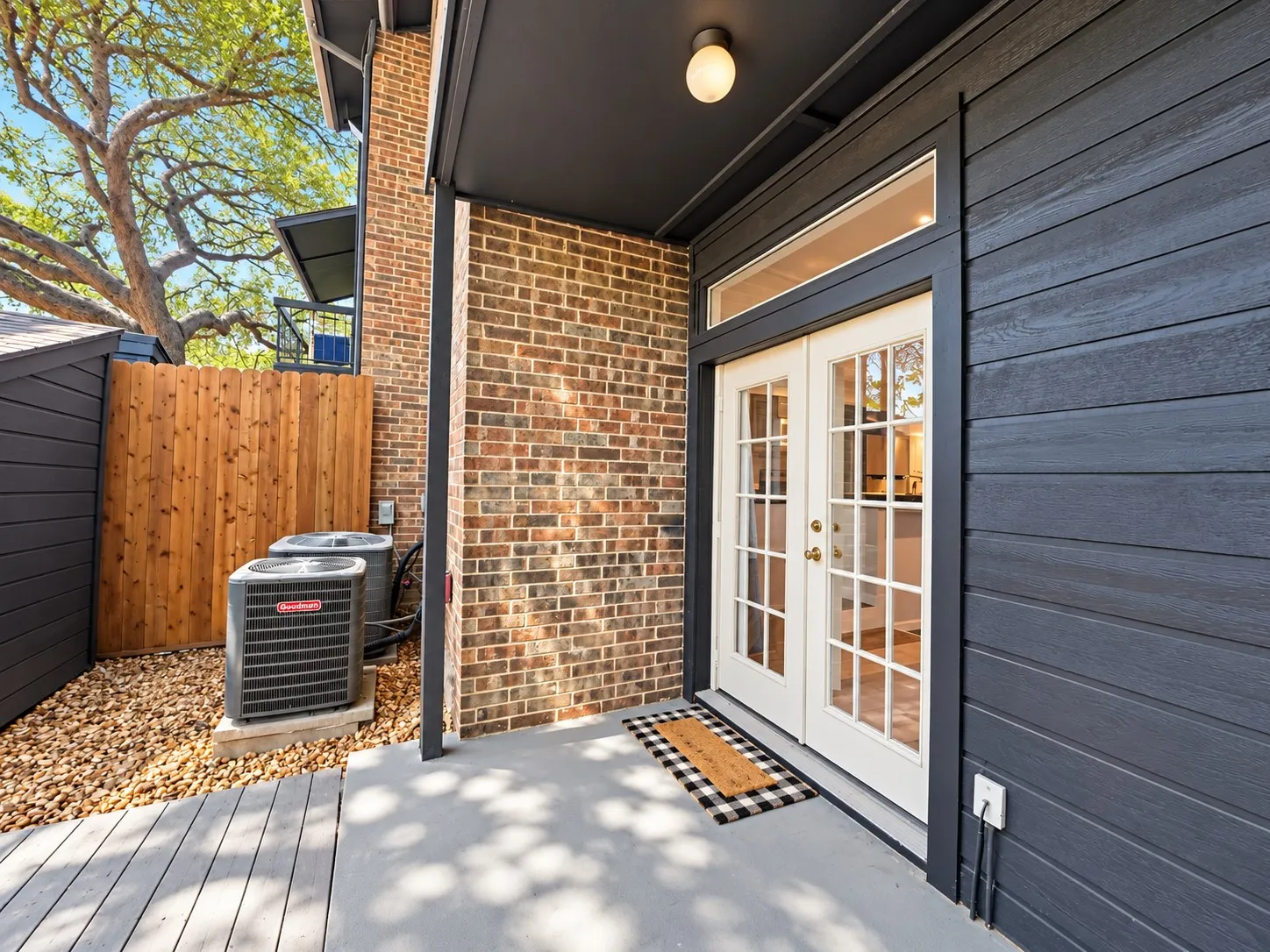 Covered exterior patio featuring horizontal siding, exposed brick masonry, French doors with glass panes, and a transom window