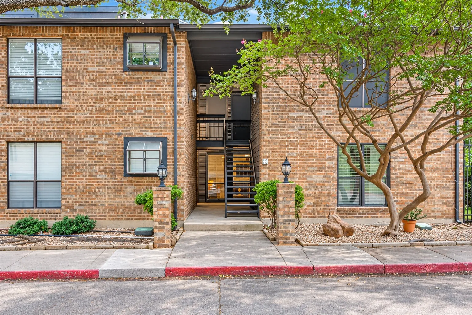 Multi-story brick exterior featuring a recessed entrance, black metal staircase, multi-pane windows, and exterior light fixtures