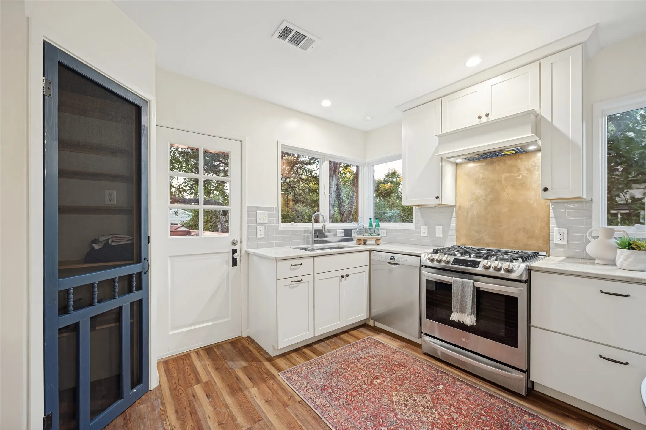 Kitchen featuring shaker-style cabinetry, stainless steel appliances, stone-finish countertops, subway tile backsplash, and wood-finish flooring
