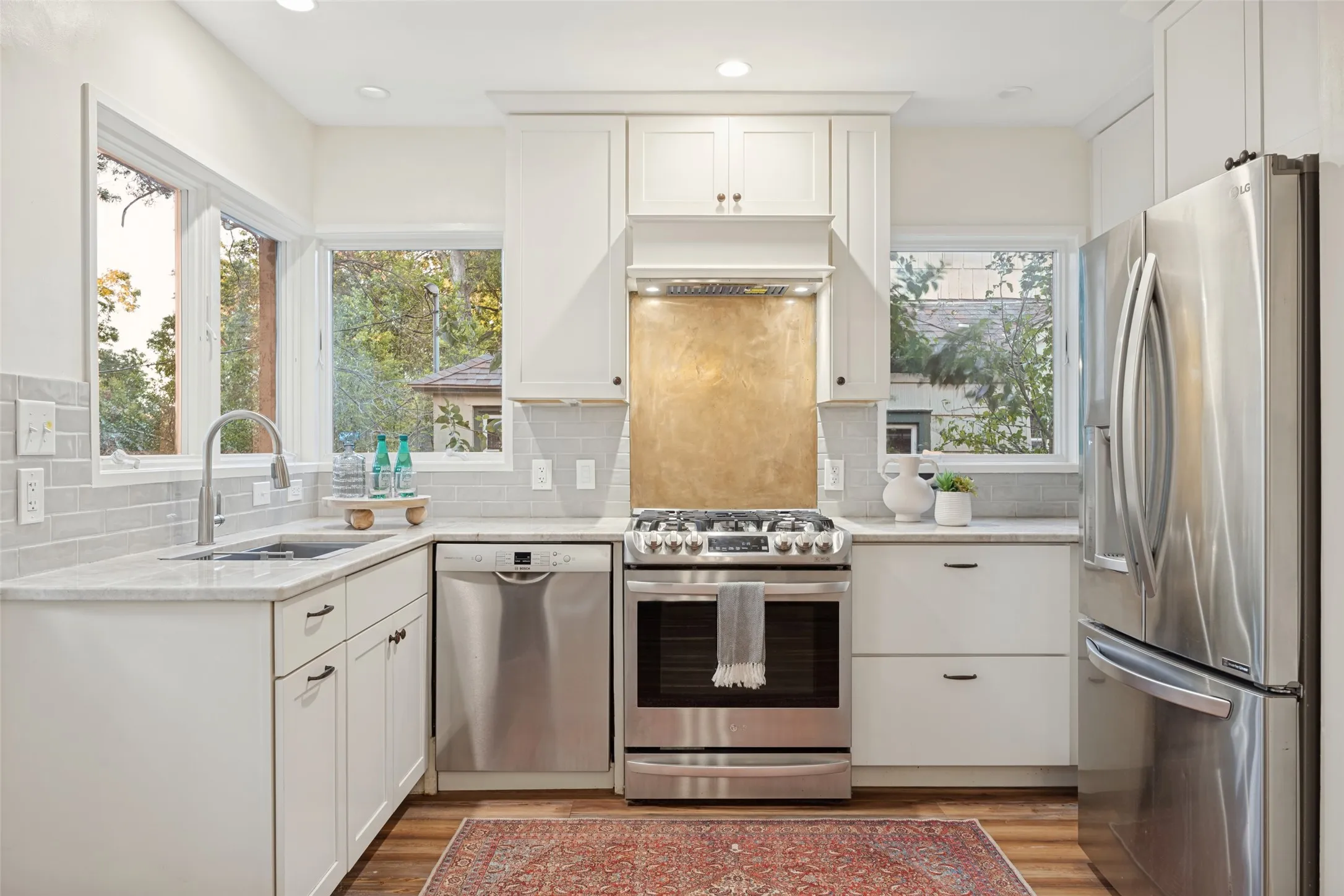 Kitchen featuring white cabinetry, stainless steel appliances, light-toned countertops, subway tile backsplash, and a metallic range backsplash
