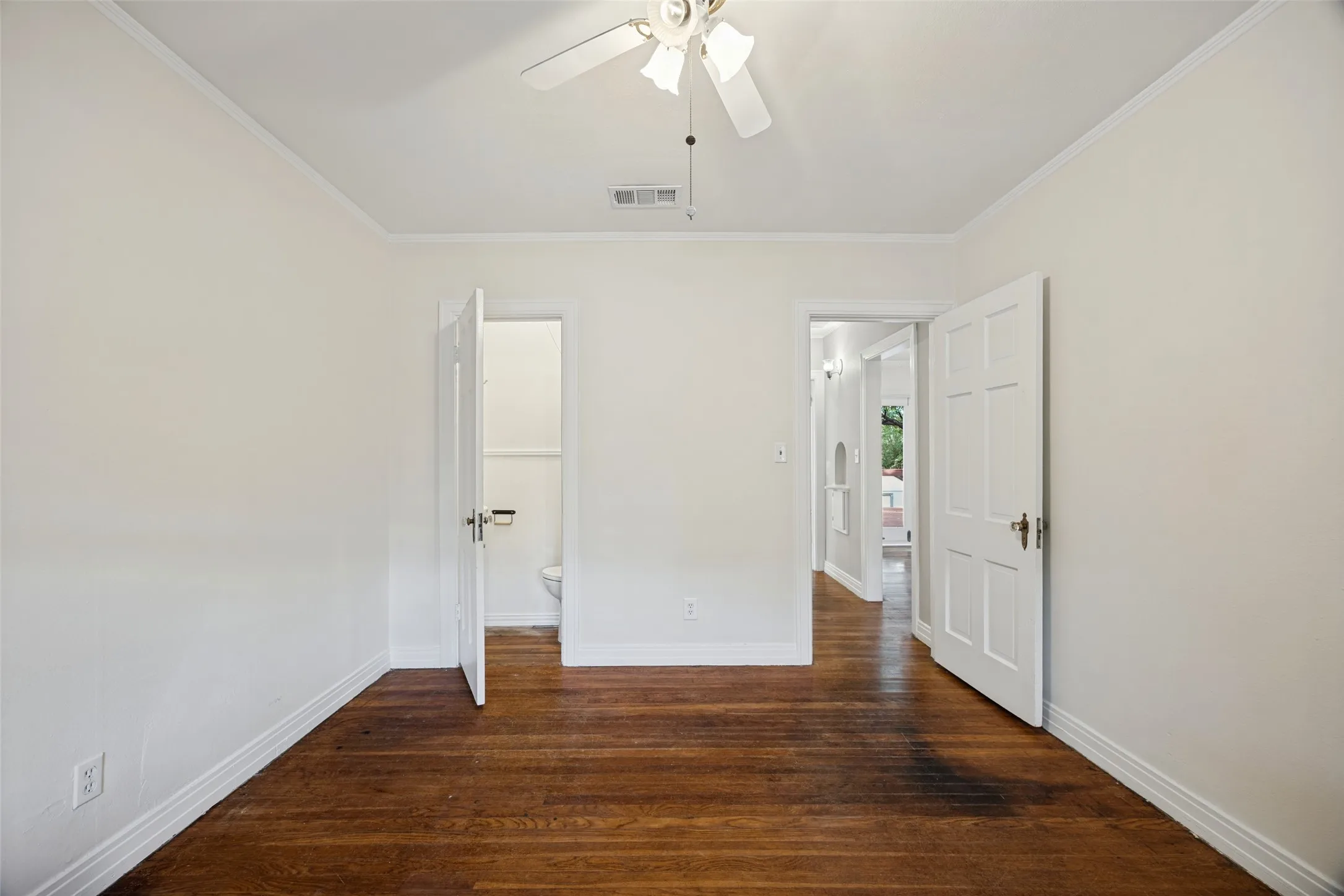 Room featuring wood-finish flooring, white six-panel interior doors, and a ceiling-mounted light fixture with a fan