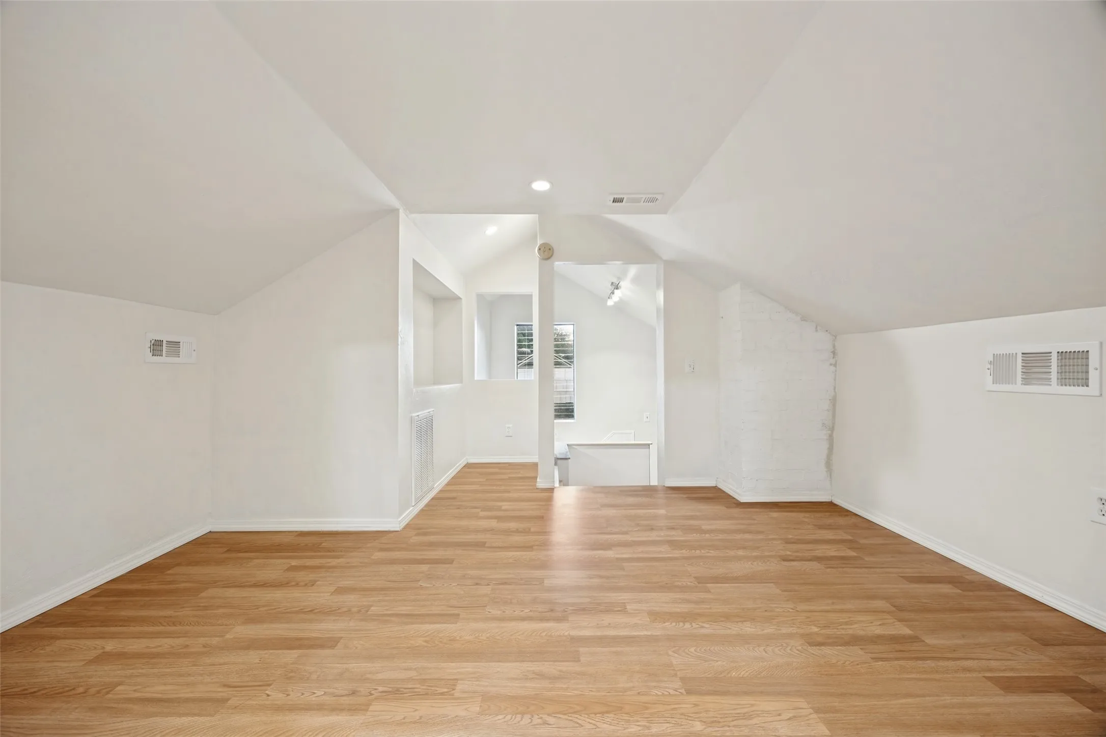 Vaulted ceilings with recessed lighting, wood-finish flooring, built-in shelving, and a painted brick accent wall