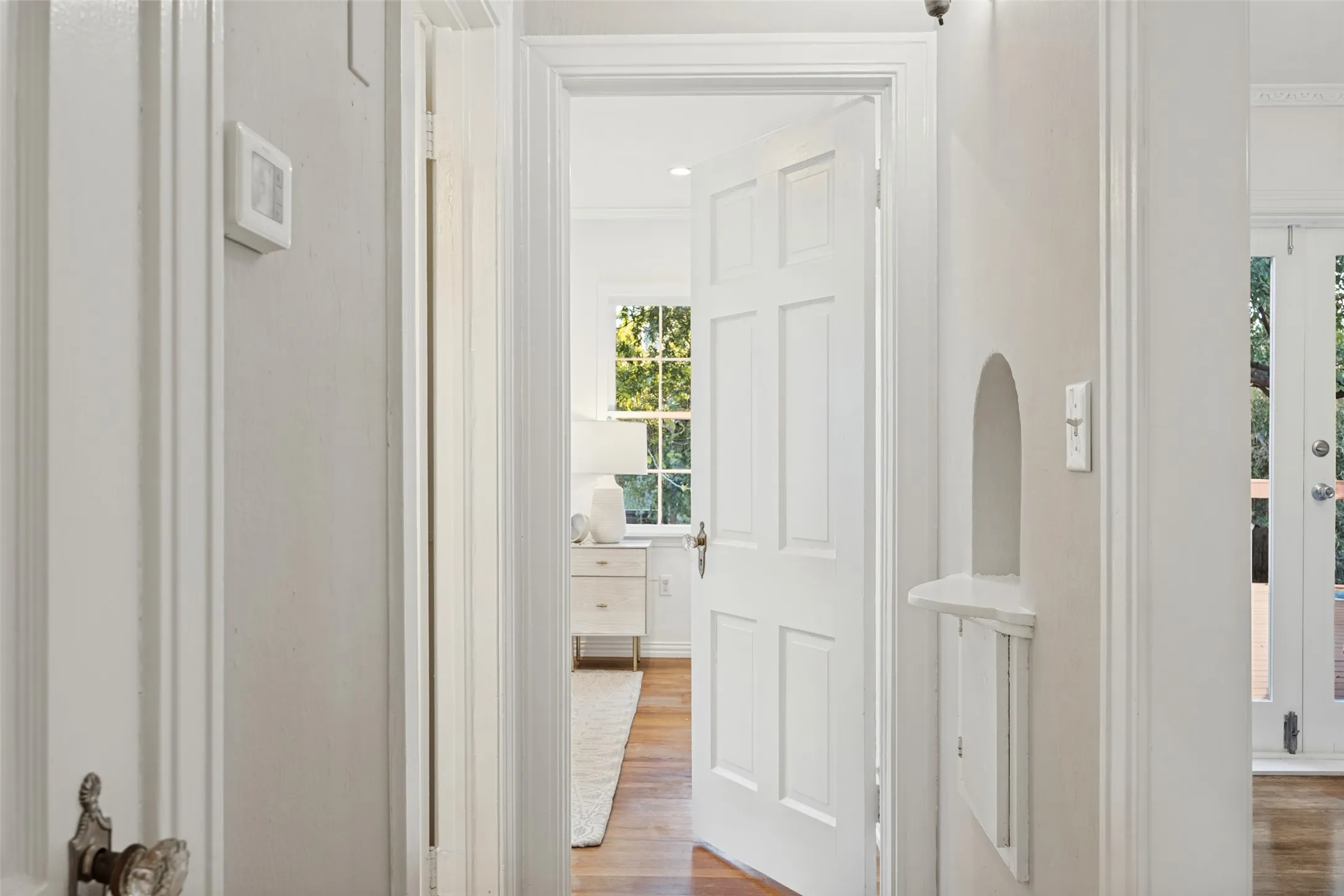 Six-panel interior door with traditional hardware, arched architectural wall niche, wood-finish flooring, and double-paned multi-light window