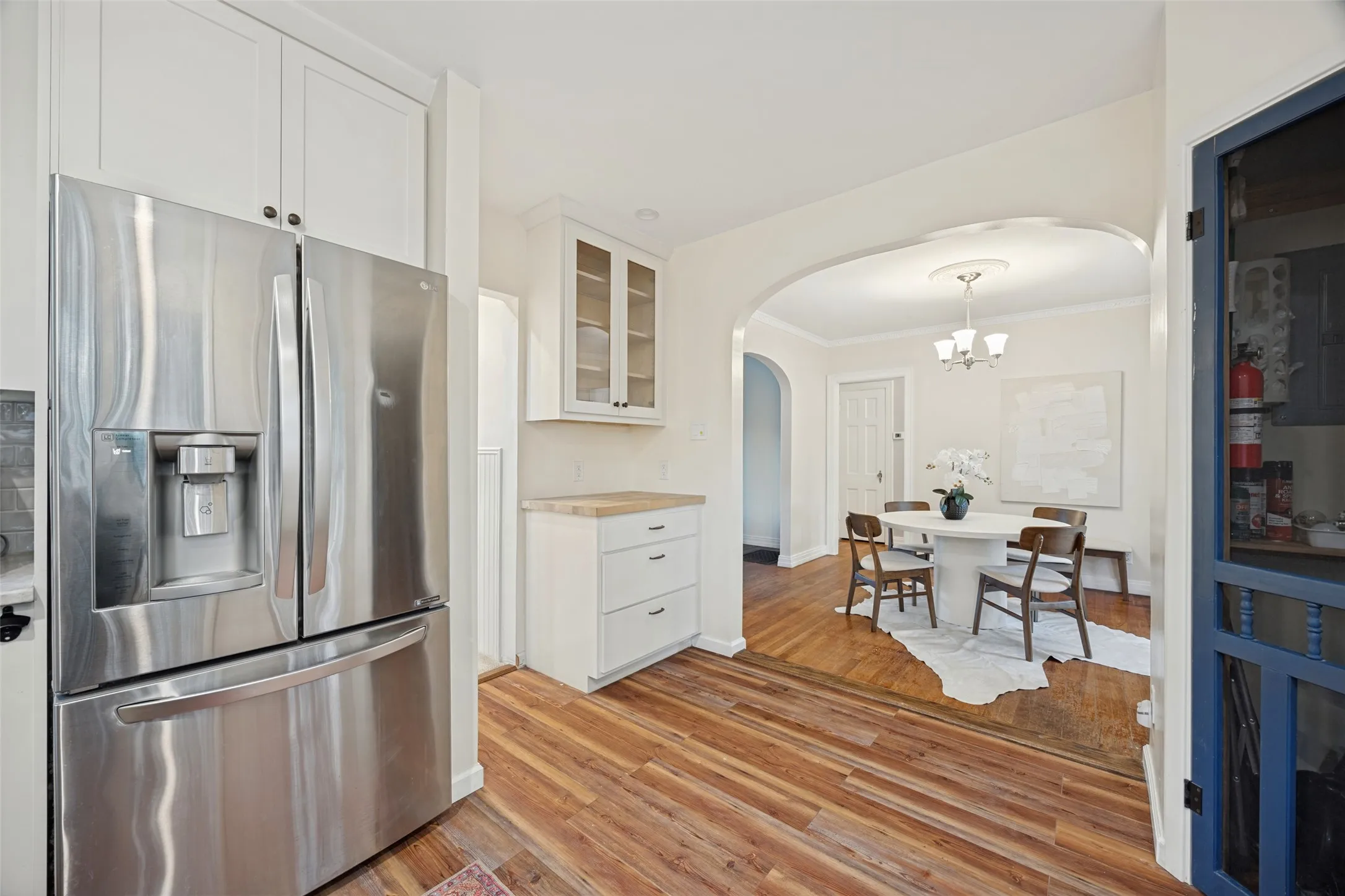 Kitchen featuring white cabinetry with glass-front display uppers, wood-finish flooring, and stainless steel refrigerator