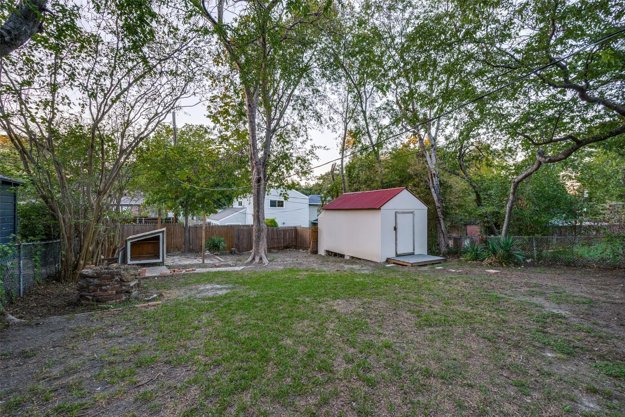 Spacious backyard featuring mature trees, a detached storage structure with a metal roof, and perimeter fencing