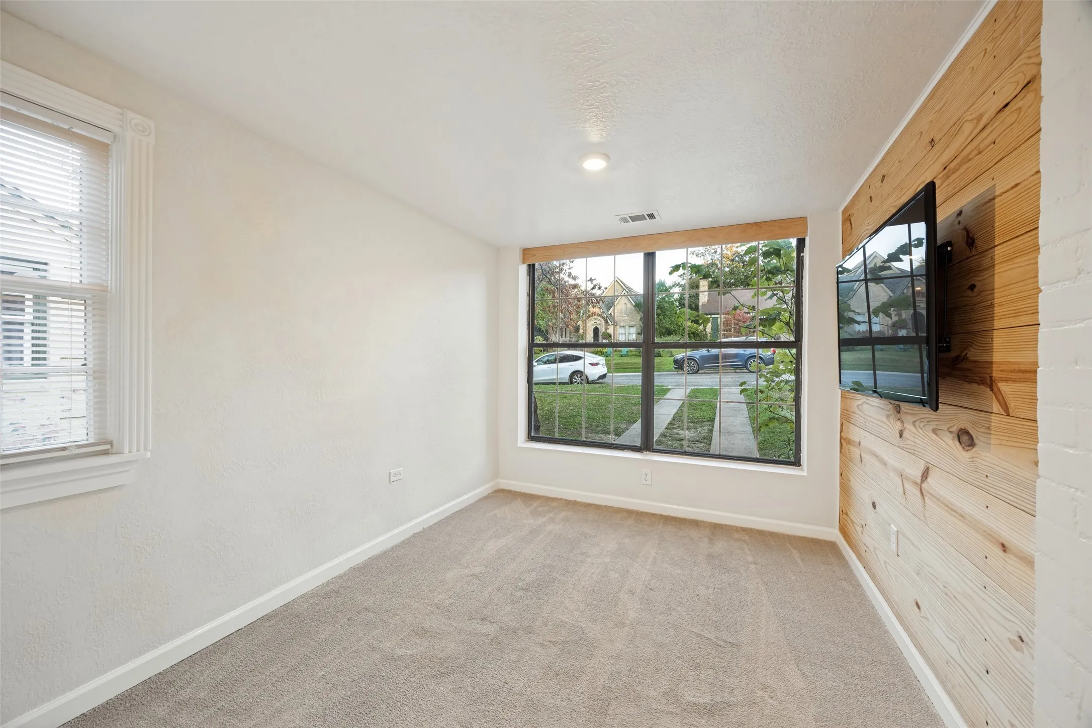 Room featuring a natural wood-plank accent wall, large picture window with dark framing, neutral wall-to-wall carpeting, and recessed lighting