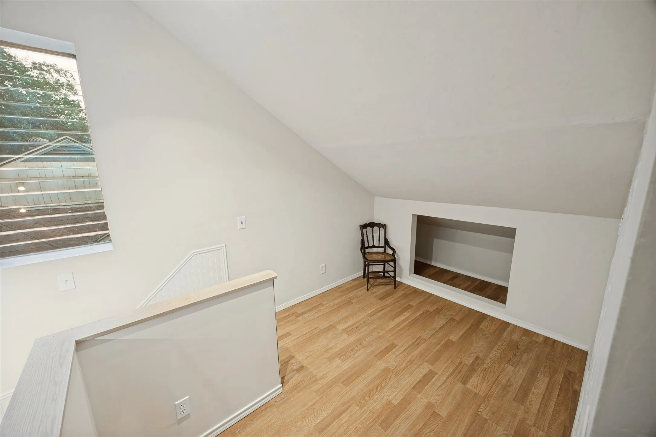Interior space featuring vaulted ceilings, wood-finish flooring, a rectangular wall-recessed storage area, and a large window