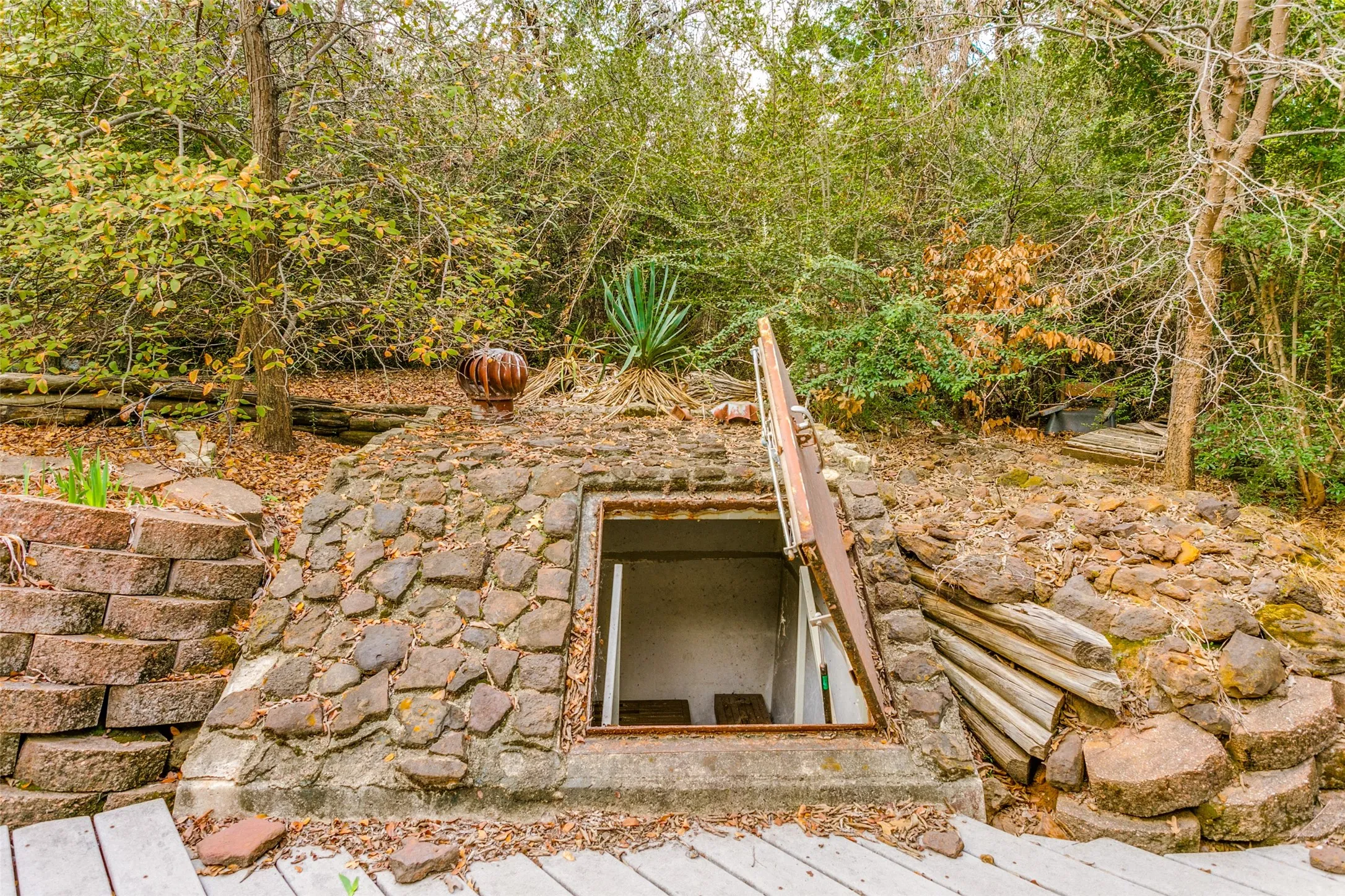 Outdoor stone storm cellar featuring a metal entry door and reinforced stone retaining walls