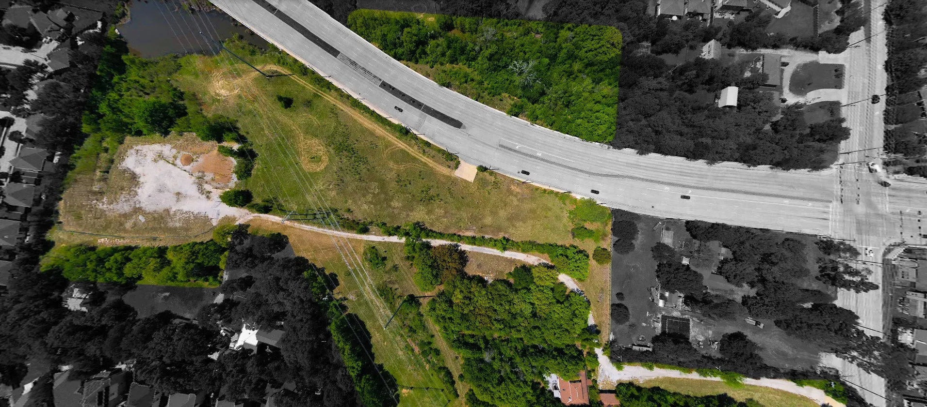 Expansive land parcel featuring a mix of cleared and treed areas, bordered by a multi-lane roadway and a body of water