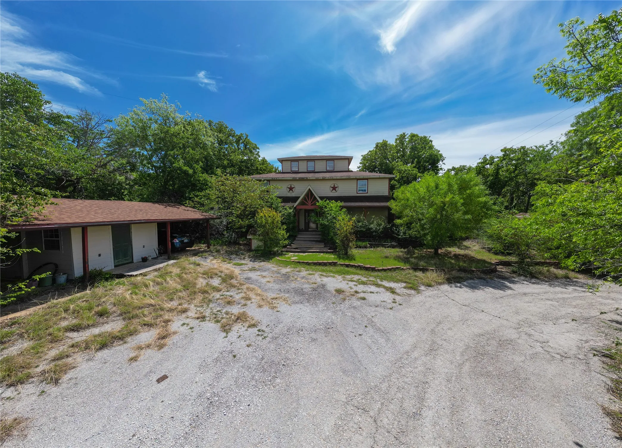 Terraced property featuring a multi-story main residence with a prominent entryway, a detached single-story structure with an extended covered area, and a substantial gravel and paved driveway