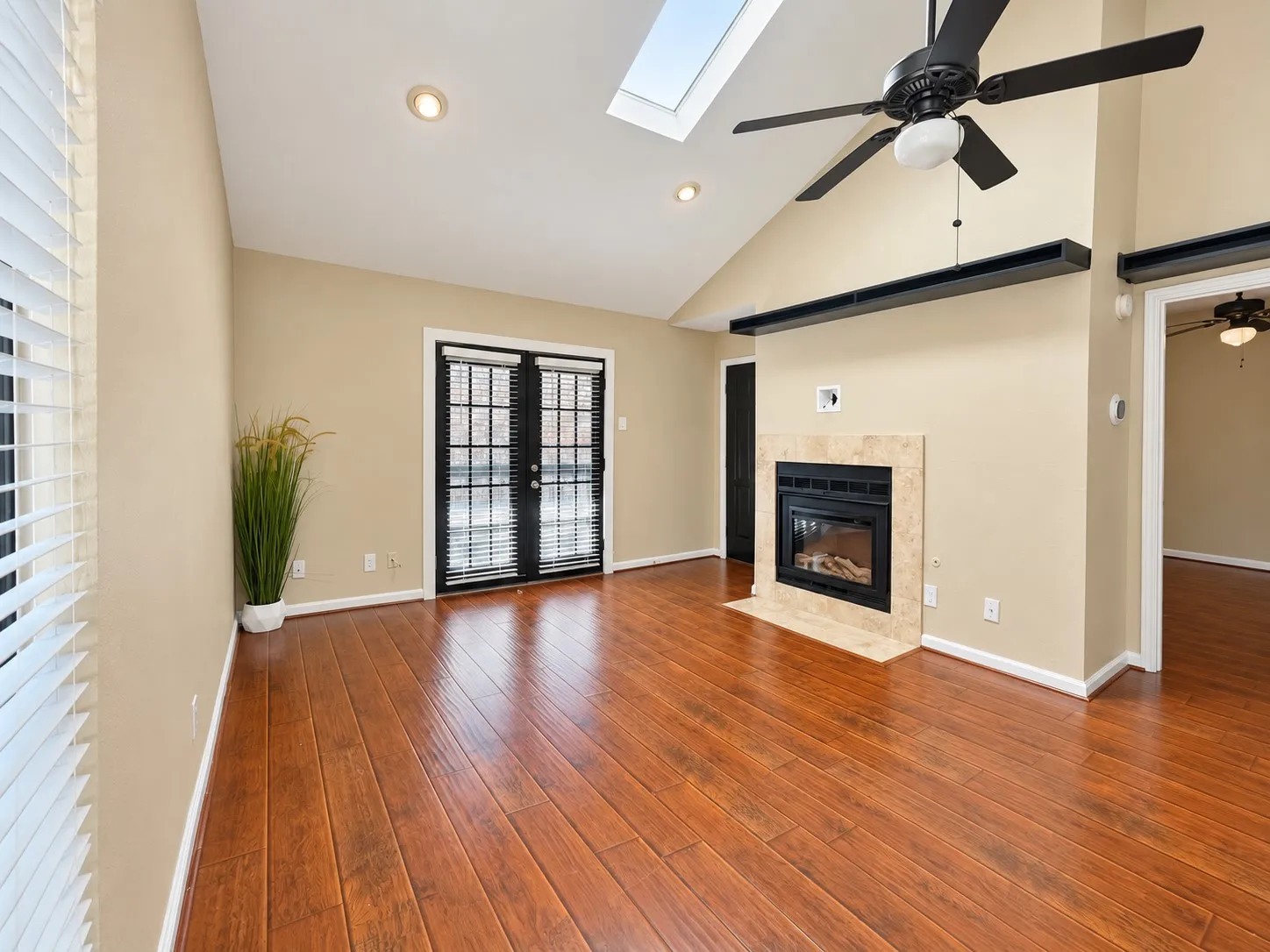 Vaulted ceiling featuring a skylight, wood-finish flooring, fireplace with a tiled surround, and black-framed French doors