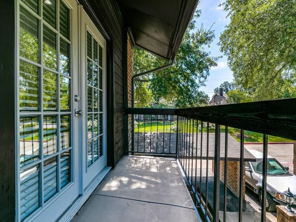 Covered balcony featuring white-frame French doors, concrete flooring, and black metal railings