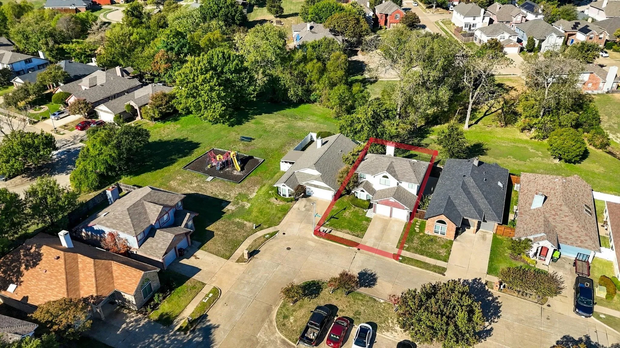 Aerial view of a residential property featuring a pitched shingle roof, integrated two-car garage, concrete driveway, and a fenced backyard