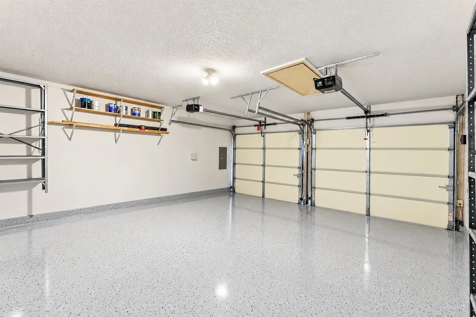 Two-car garage featuring epoxy-coated flooring, built-in wall shelving, an automatic door opener system, and attic access
