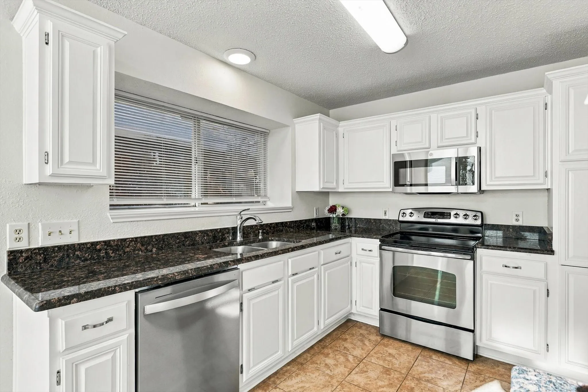 Kitchen featuring white cabinetry, stone countertops, stainless steel appliances, and ceramic tile flooring