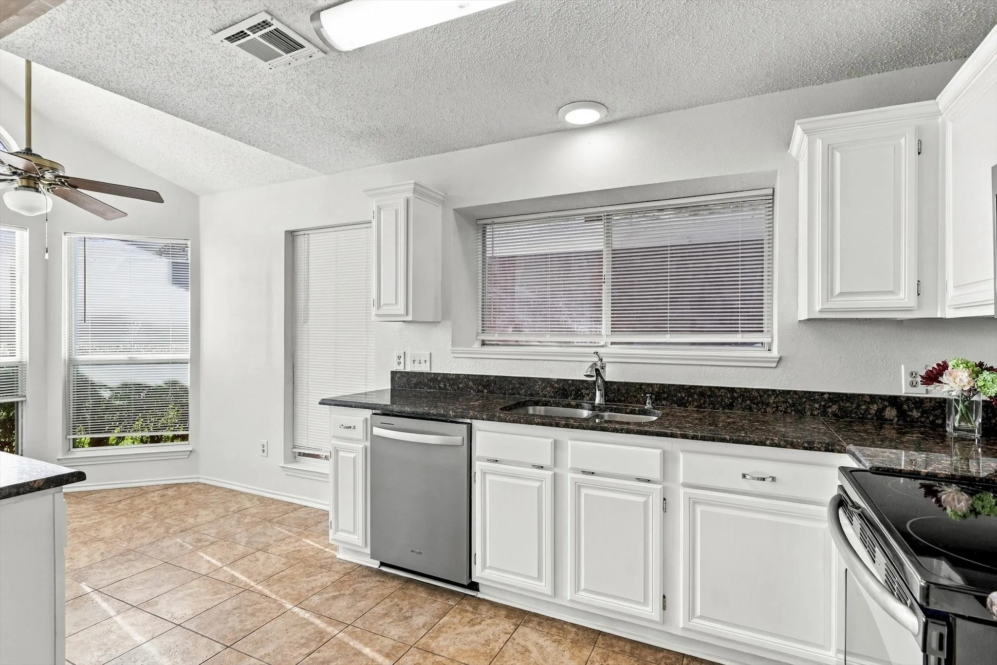 Kitchen featuring white shaker-style cabinetry, stone countertops, stainless steel dishwasher, tile flooring, and vaulted ceilings