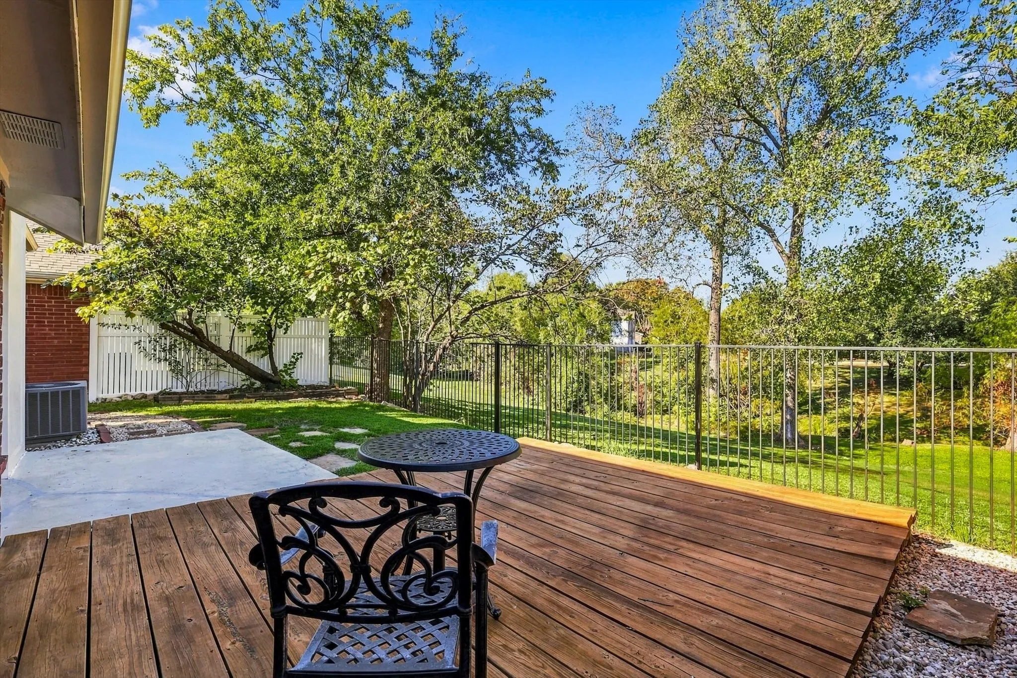 Wood deck, concrete patio, metal perimeter fencing, and mature trees