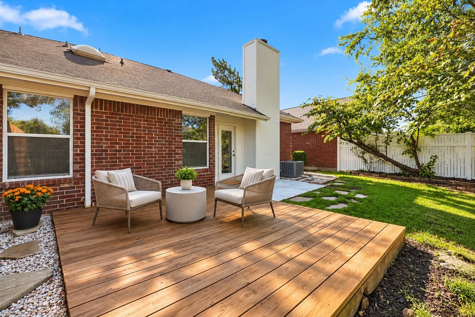 Exterior featuring a red brick facade, wood-finish decking, white chimney stack, stone paver accents, and a fenced backyard