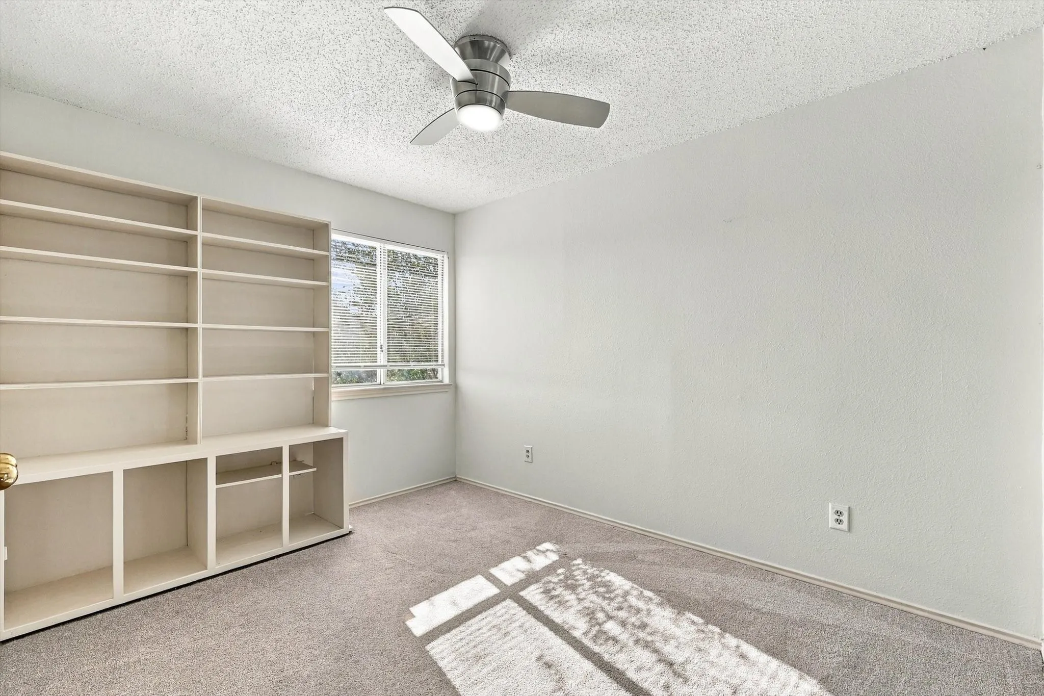 Room featuring built-in floor-to-ceiling shelving, neutral carpeting, a dual-pane window, and a ceiling fan with integrated lighting